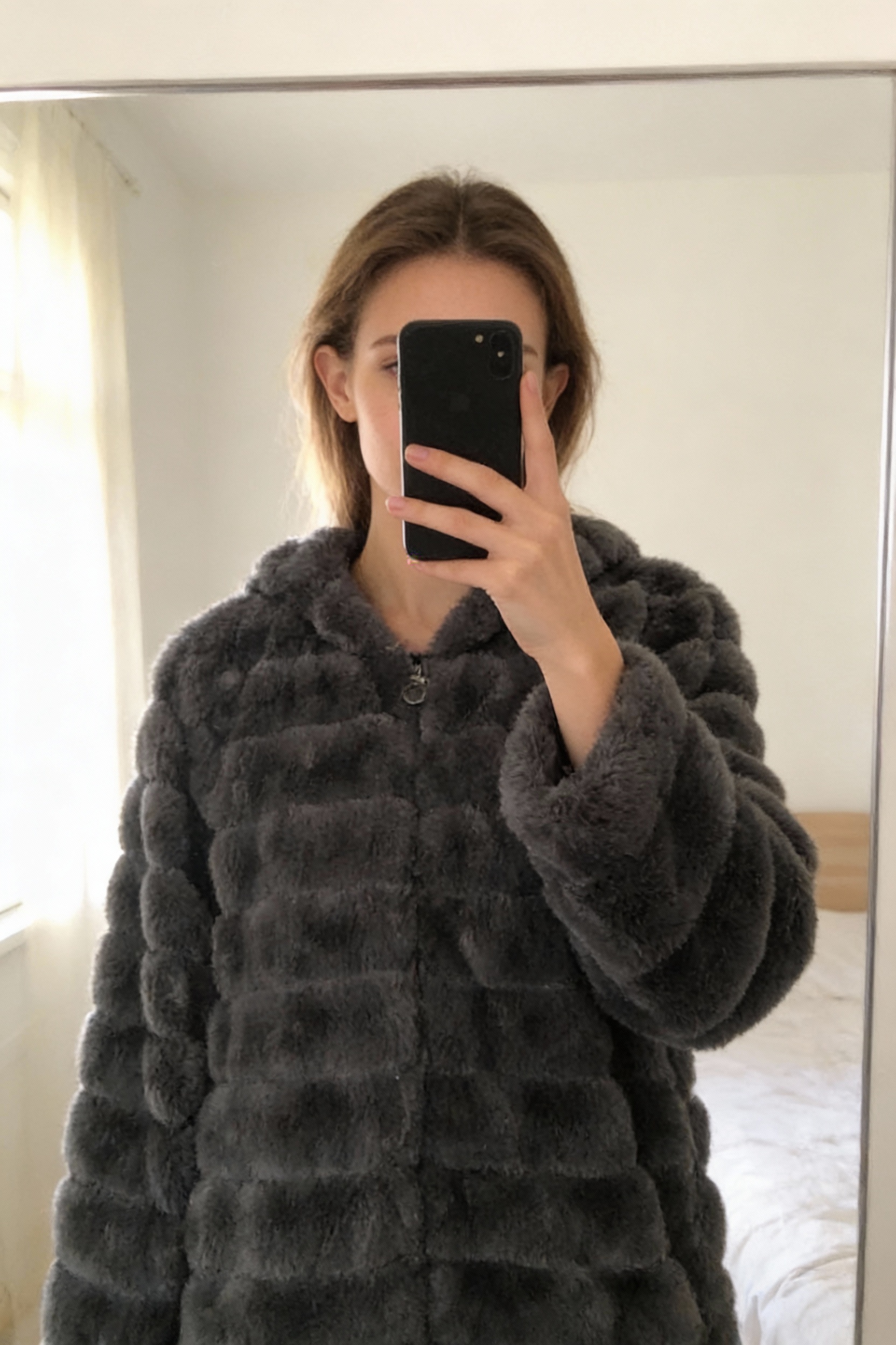 Veste à capuche debout, face à la caméra, dans une chambre à la lumière douce, avec une lumière naturelle filtrant par la fenêtre.