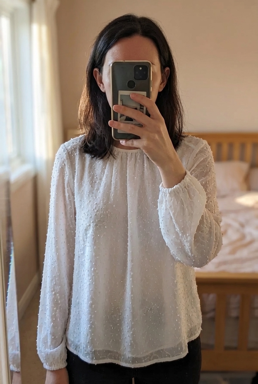 Chemisier mango debout, face à la caméra, dans une chambre à la lumière douce, avec une lumière naturelle filtrant par la fenêtre.