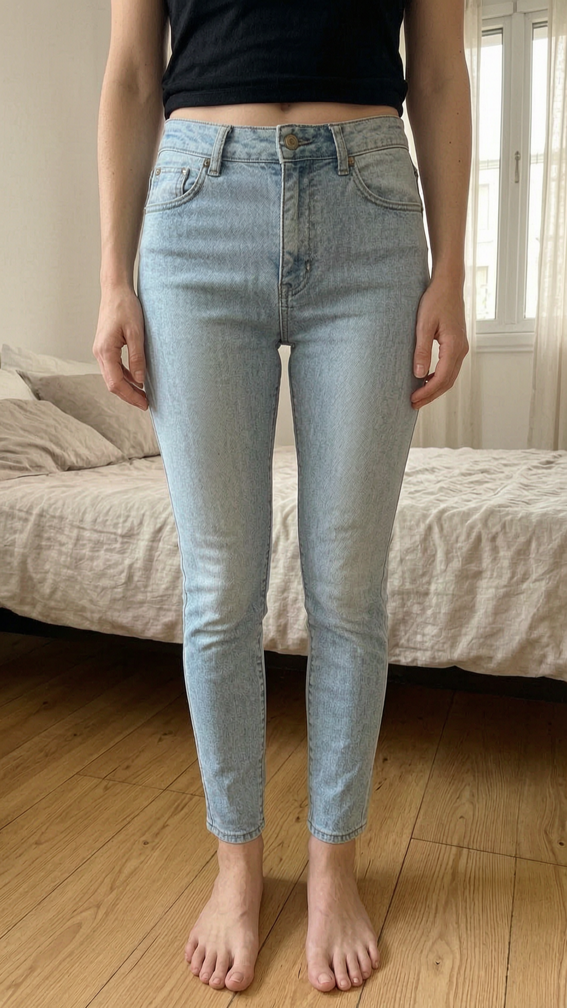 Jean clair slim tally weijl debout, face à la caméra, dans une chambre à la lumière douce, avec une lumière naturelle filtrant par la fenêtre.