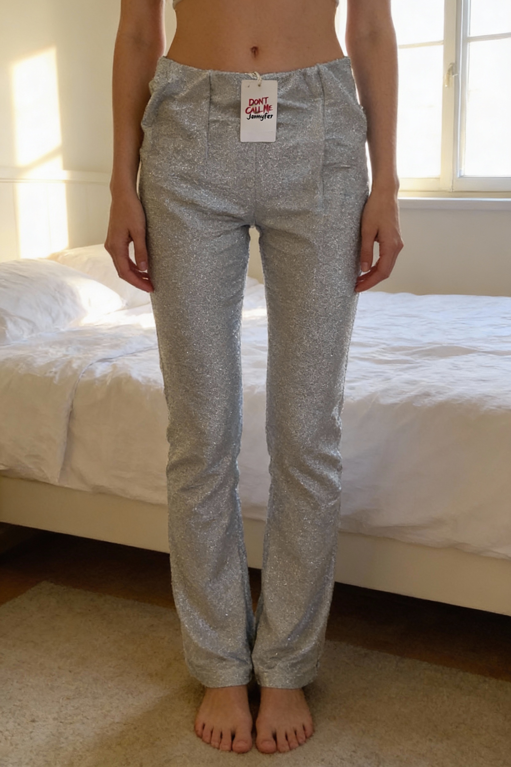 Petite jupe e debout, face à la caméra, dans une chambre à la lumière douce, avec une lumière naturelle filtrant par la fenêtre.