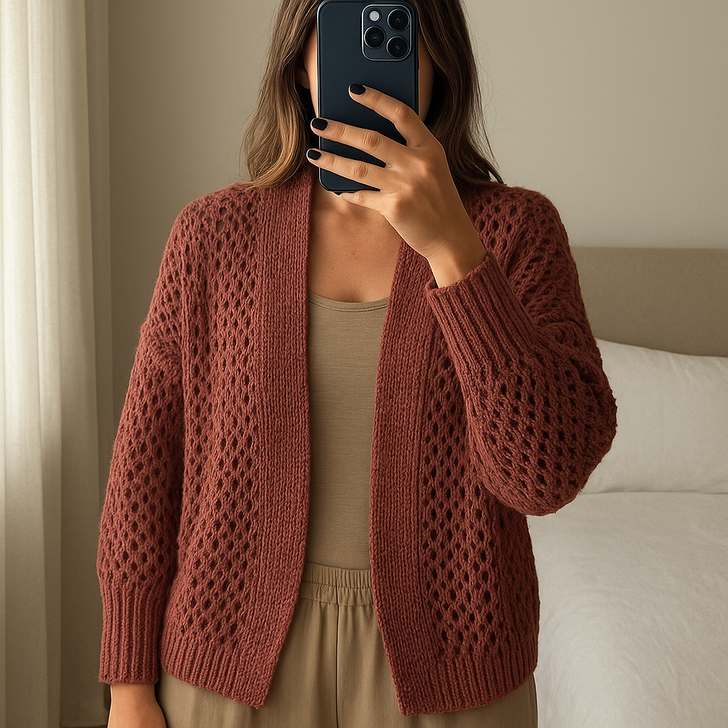 cardigan maglia larga in piedi, rivolto verso la fotocamera, in una camera da letto con luce soffusa e luce naturale che filtra dalla finestra.