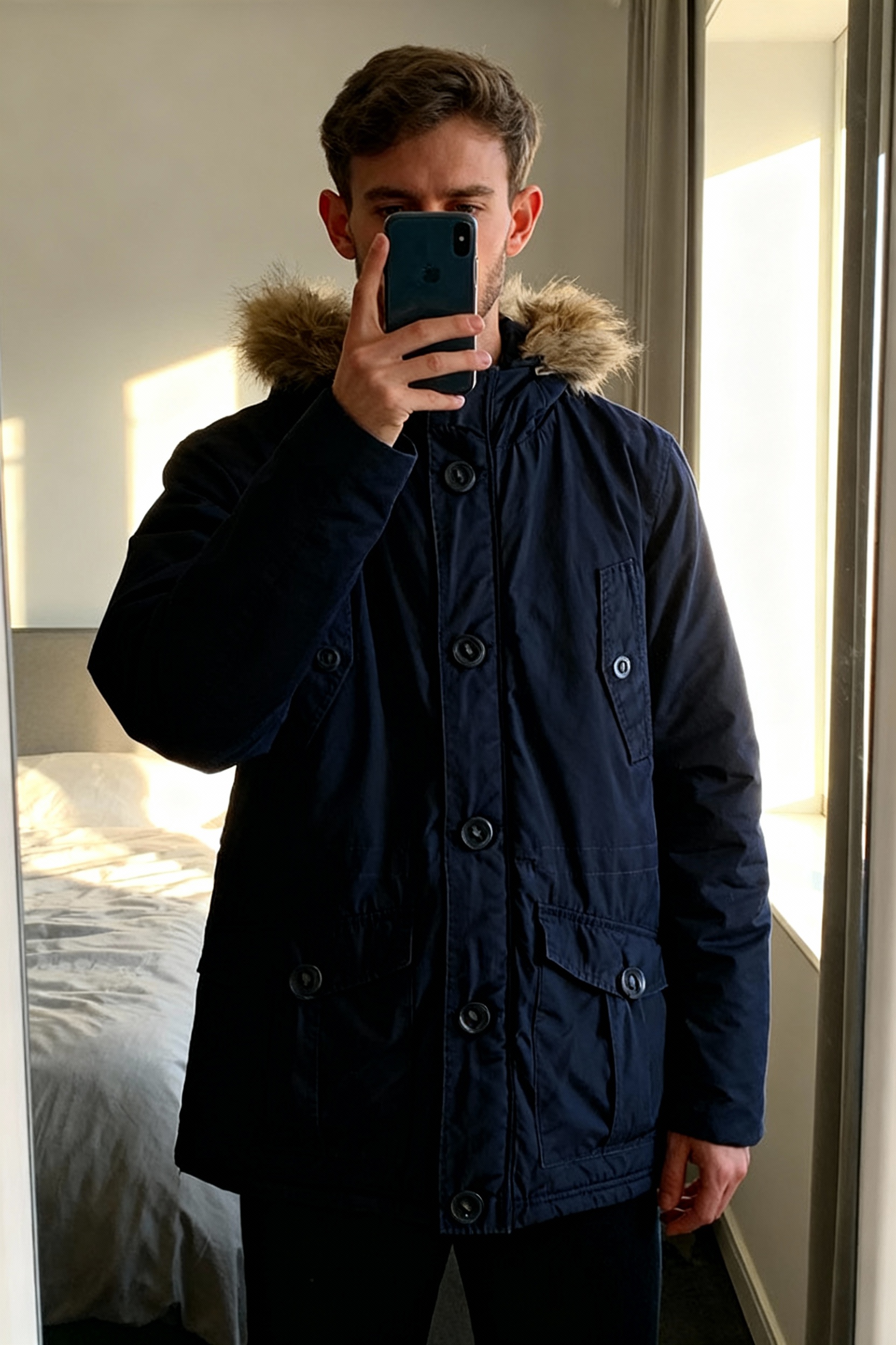 Manteau Armand Thiery debout, face à la caméra, dans une chambre à la lumière douce, avec une lumière naturelle filtrant par la fenêtre.