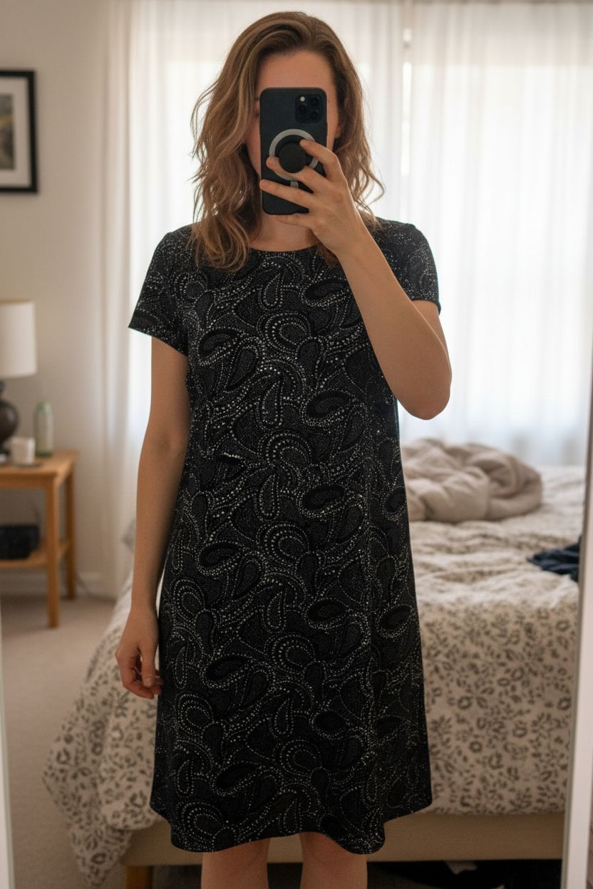 River Island black dress size 14 paisley velvet embellished shift party evening boho standing straight facing the camera, in a softly lit bedroom setting, with gentle natural light filtering through a window.