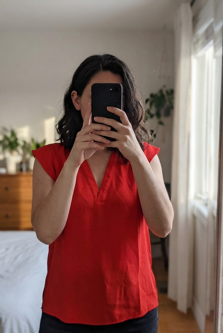 Blouse rouge fluide à col v Zara taille M debout, face à la caméra, dans une chambre à la lumière douce, avec une lumière naturelle filtrant par la fenêtre.