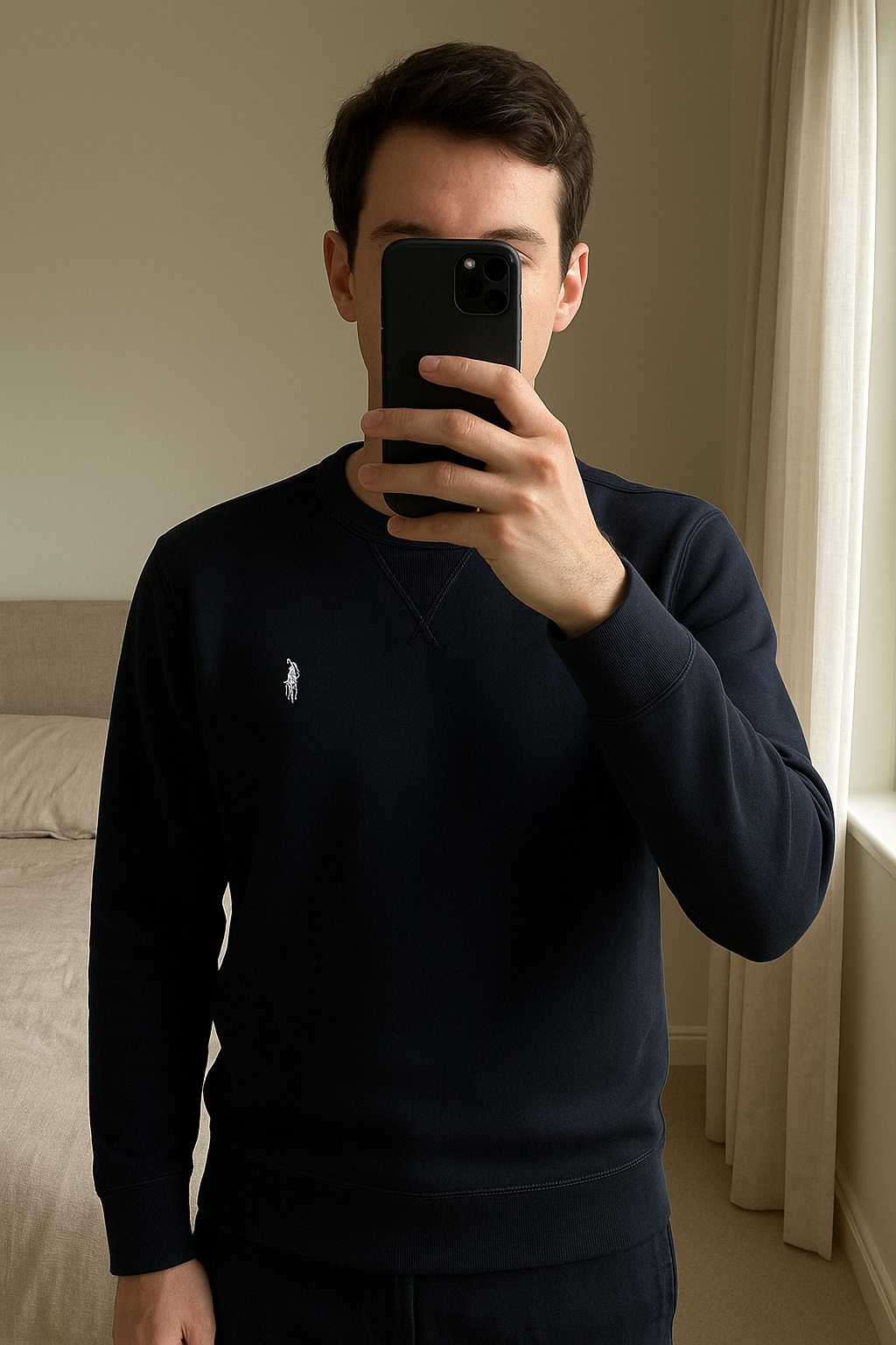 Pull Ralph Lauren debout, face à la caméra, dans une chambre à la lumière douce, avec une lumière naturelle filtrant par la fenêtre.
