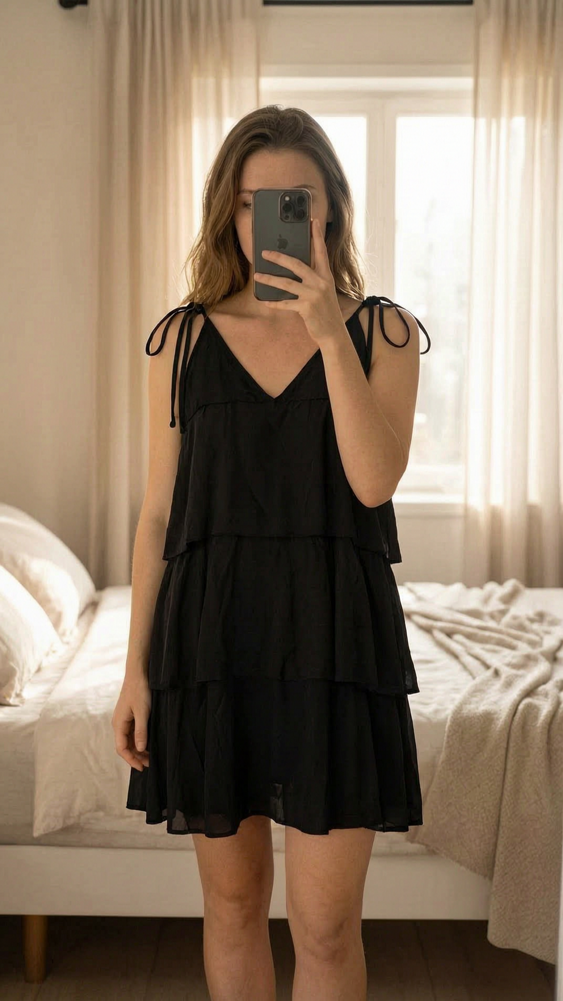 Robe à volant à nouer au cou TU debout, face à la caméra, dans une chambre à la lumière douce, avec une lumière naturelle filtrant par la fenêtre.