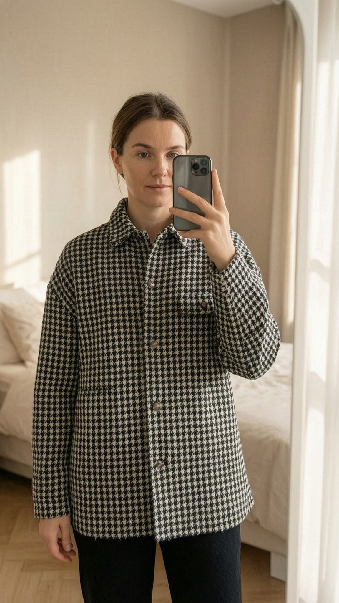 Veste gilet noir et blanc debout, face à la caméra, dans une chambre à la lumière douce, avec une lumière naturelle filtrant par la fenêtre.