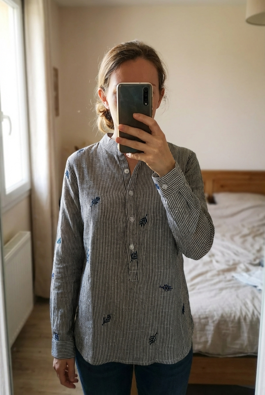Chemise debout, face à la caméra, dans une chambre à la lumière douce, avec une lumière naturelle filtrant par la fenêtre.
