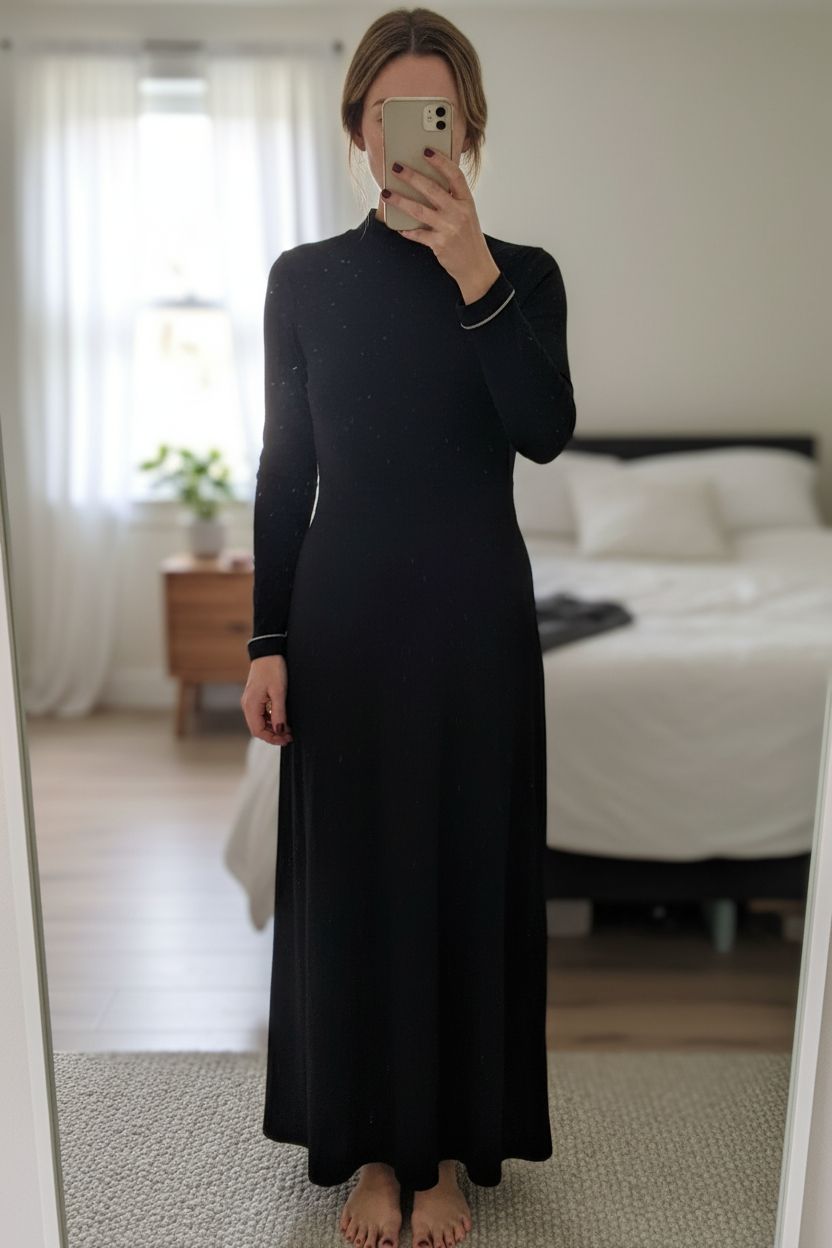 Religion Backless Full Length Dress standing straight facing the camera, in a softly lit bedroom setting, with gentle natural light filtering through a window.