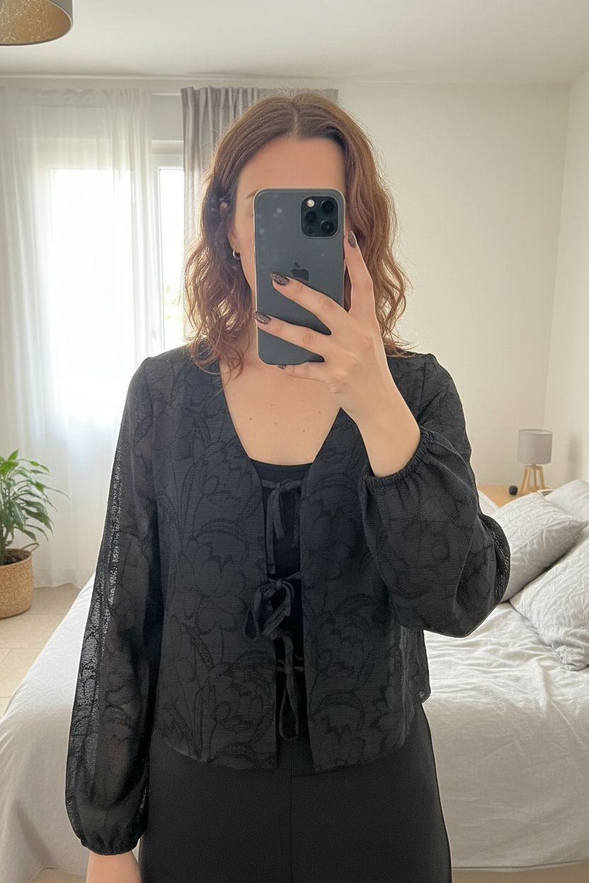 Boléro dentelle debout, face à la caméra, dans une chambre à la lumière douce, avec une lumière naturelle filtrant par la fenêtre.