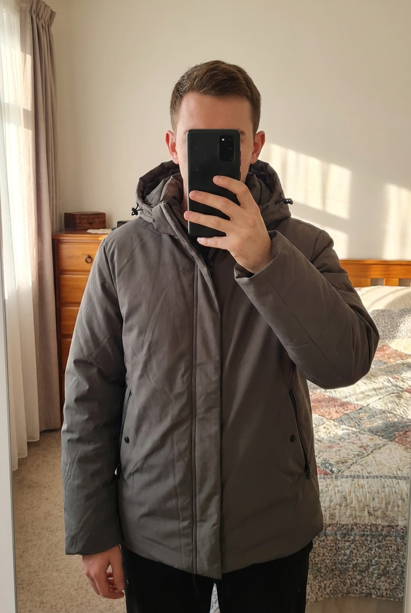 Manteau debout, face à la caméra, dans une chambre à la lumière douce, avec une lumière naturelle filtrant par la fenêtre.