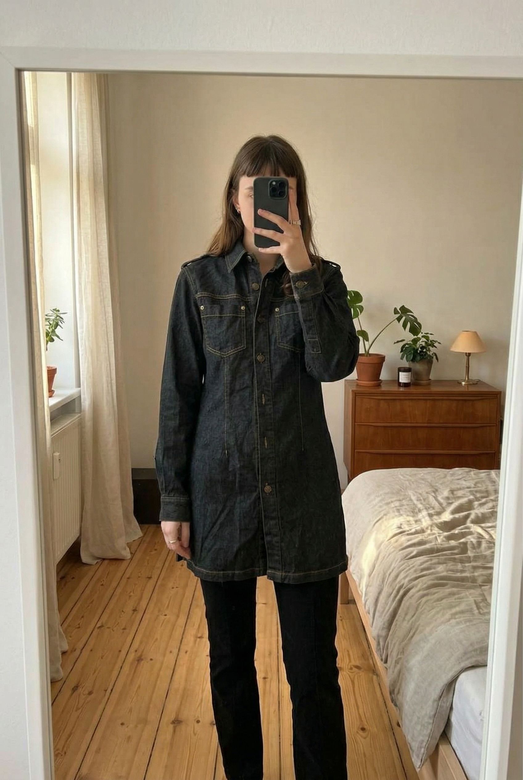 True vintage long denim shirt / mini dress aufrecht stehend, der Kamera zugewandt, in einem sanft beleuchteten Schlafzimmer, mit natürlichem Licht, das durch ein Fenster fällt.