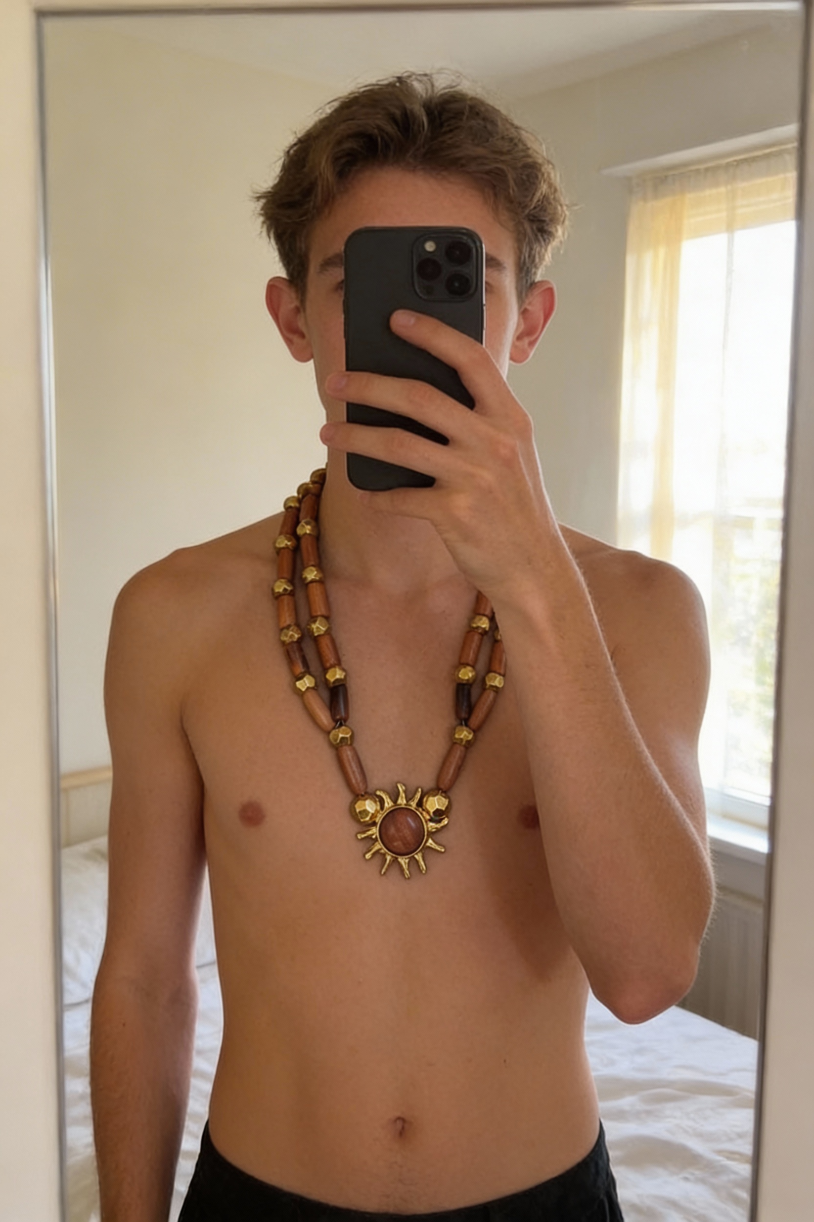 Collier vintage en bois et métal doré – Edouard Rambaud debout, face à la caméra, dans une chambre à la lumière douce, avec une lumière naturelle filtrant par la fenêtre.