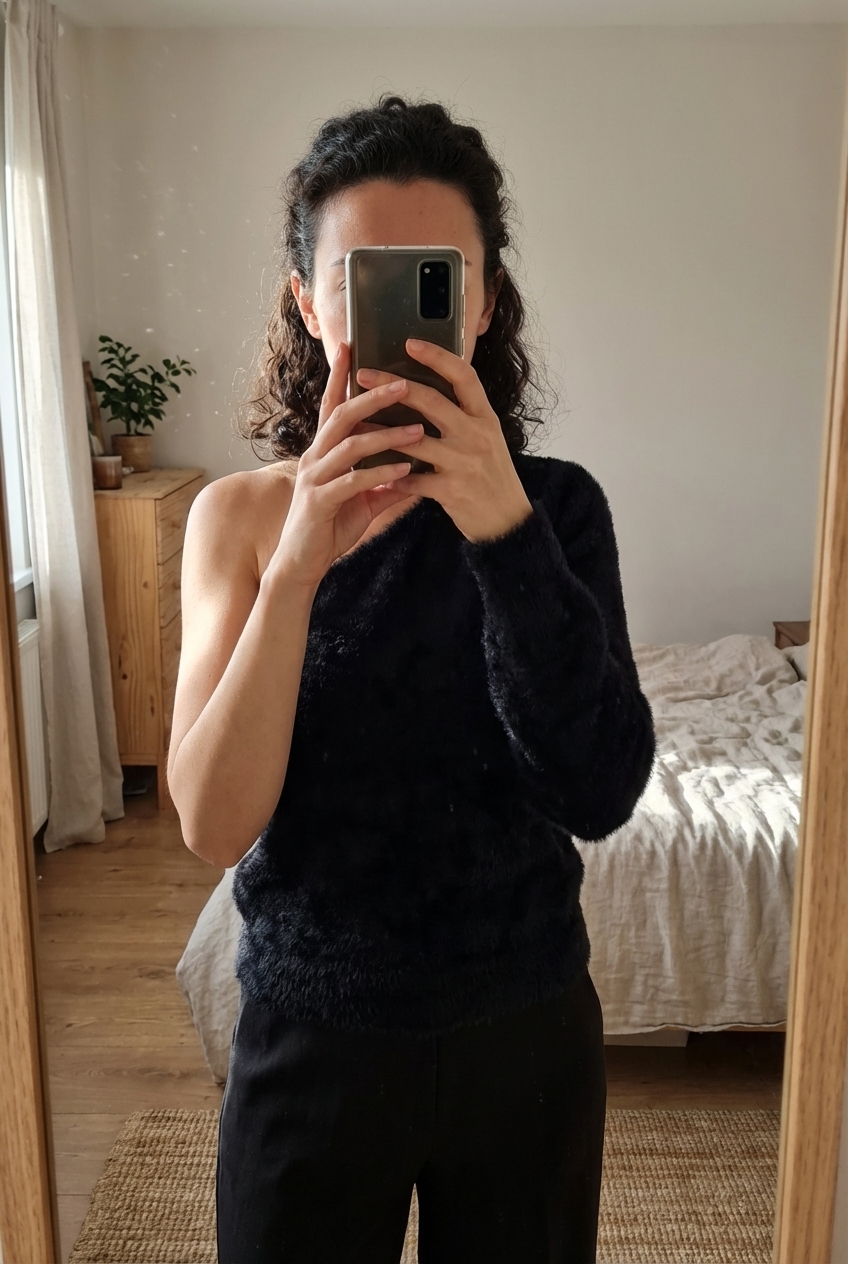 Top asymétrique Mango S debout, face à la caméra, dans une chambre à la lumière douce, avec une lumière naturelle filtrant par la fenêtre.