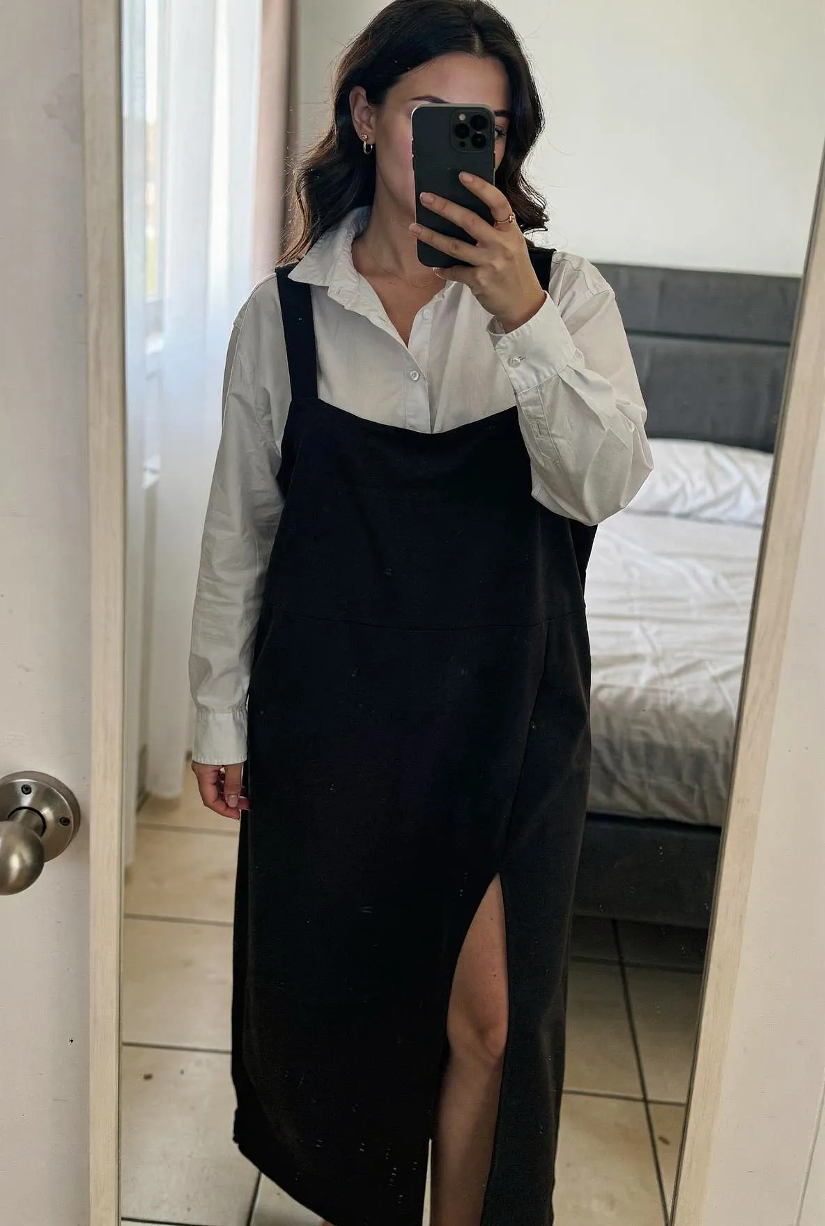 Robe longue et chemise debout, face à la caméra, dans une chambre à la lumière douce, avec une lumière naturelle filtrant par la fenêtre.