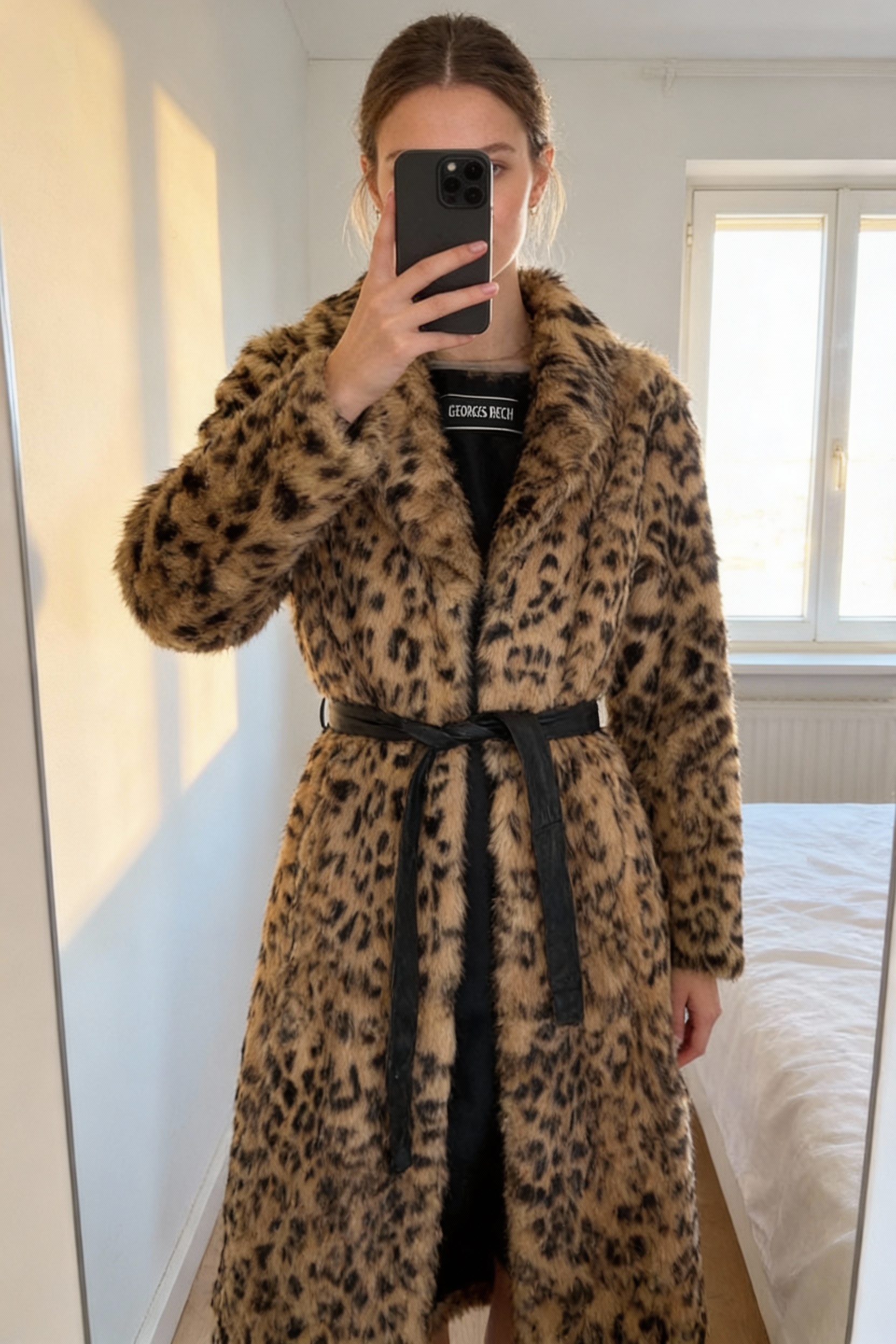 Manteau Georges Rech fourrure synthétique léopard vintage debout, face à la caméra, dans une chambre à la lumière douce, avec une lumière naturelle filtrant par la fenêtre.