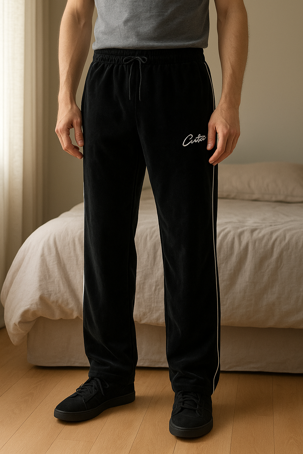 Corteiz VVS Velour Bottoms debout, face à la caméra, dans une chambre à la lumière douce, avec une lumière naturelle filtrant par la fenêtre.