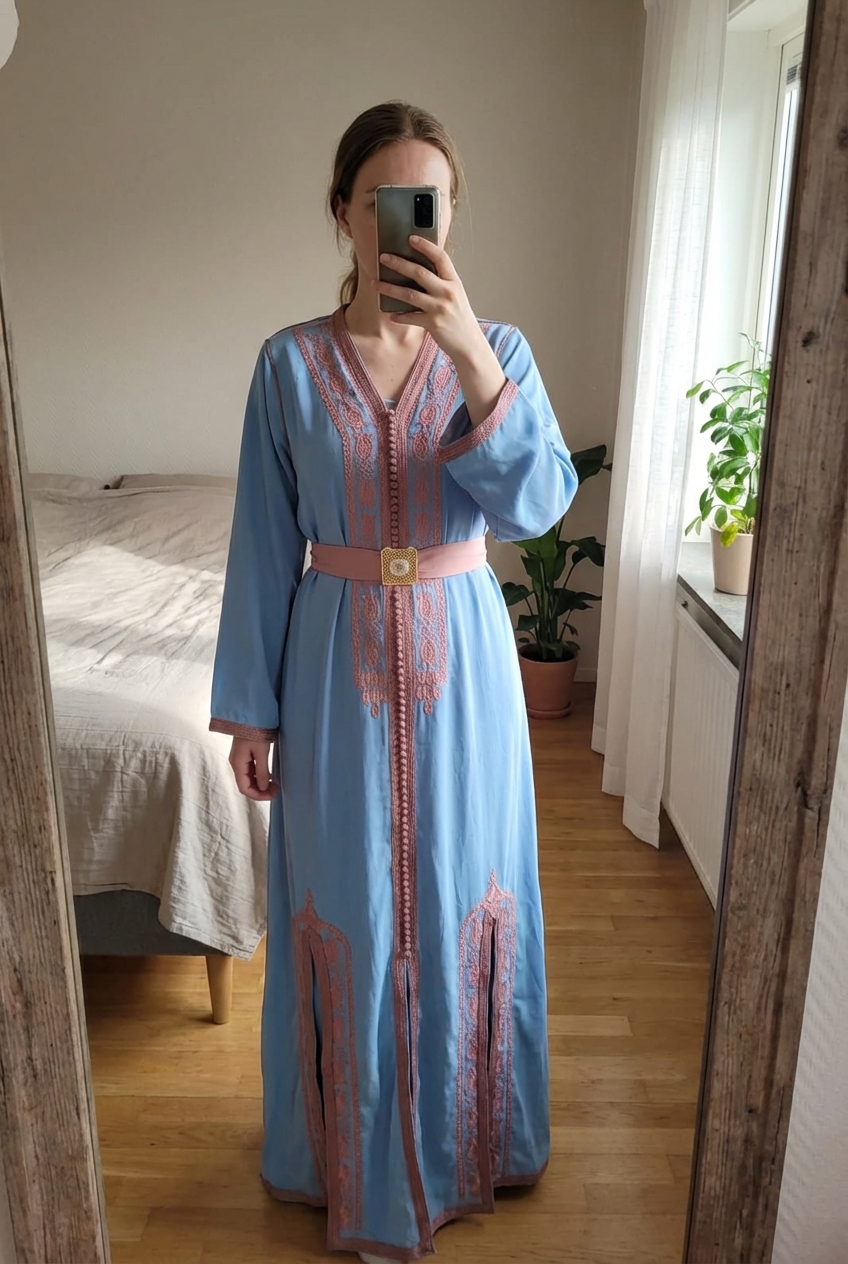 Robe Traditionnelle Marocaine Double Couche Caftan Plus Ceinture Traditionnelle debout, face à la caméra, dans une chambre à la lumière douce, avec une lumière naturelle filtrant par la fenêtre.