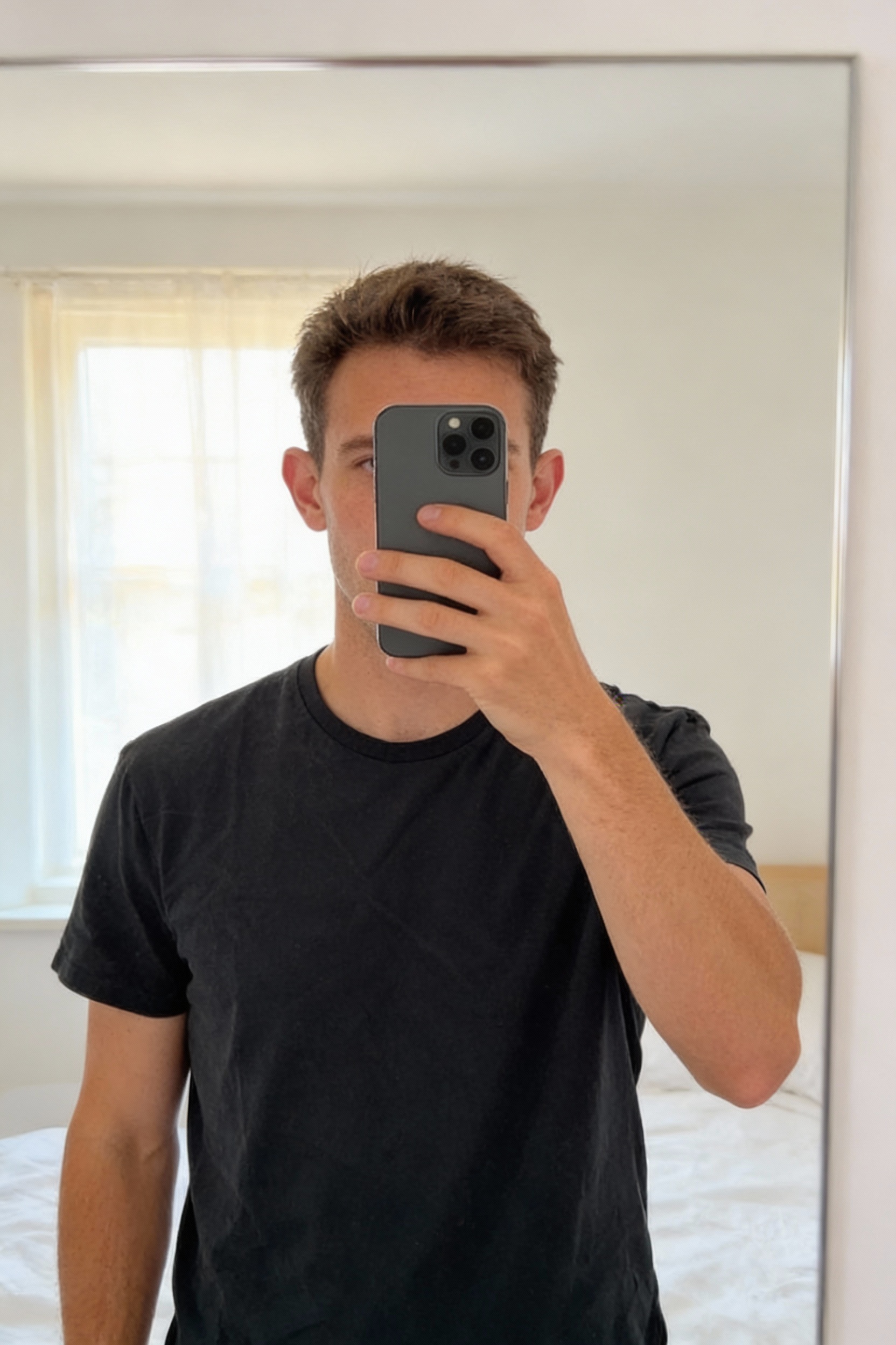 T-shirt Jetty Noir Uni debout, face à la caméra, dans une chambre à la lumière douce, avec une lumière naturelle filtrant par la fenêtre.