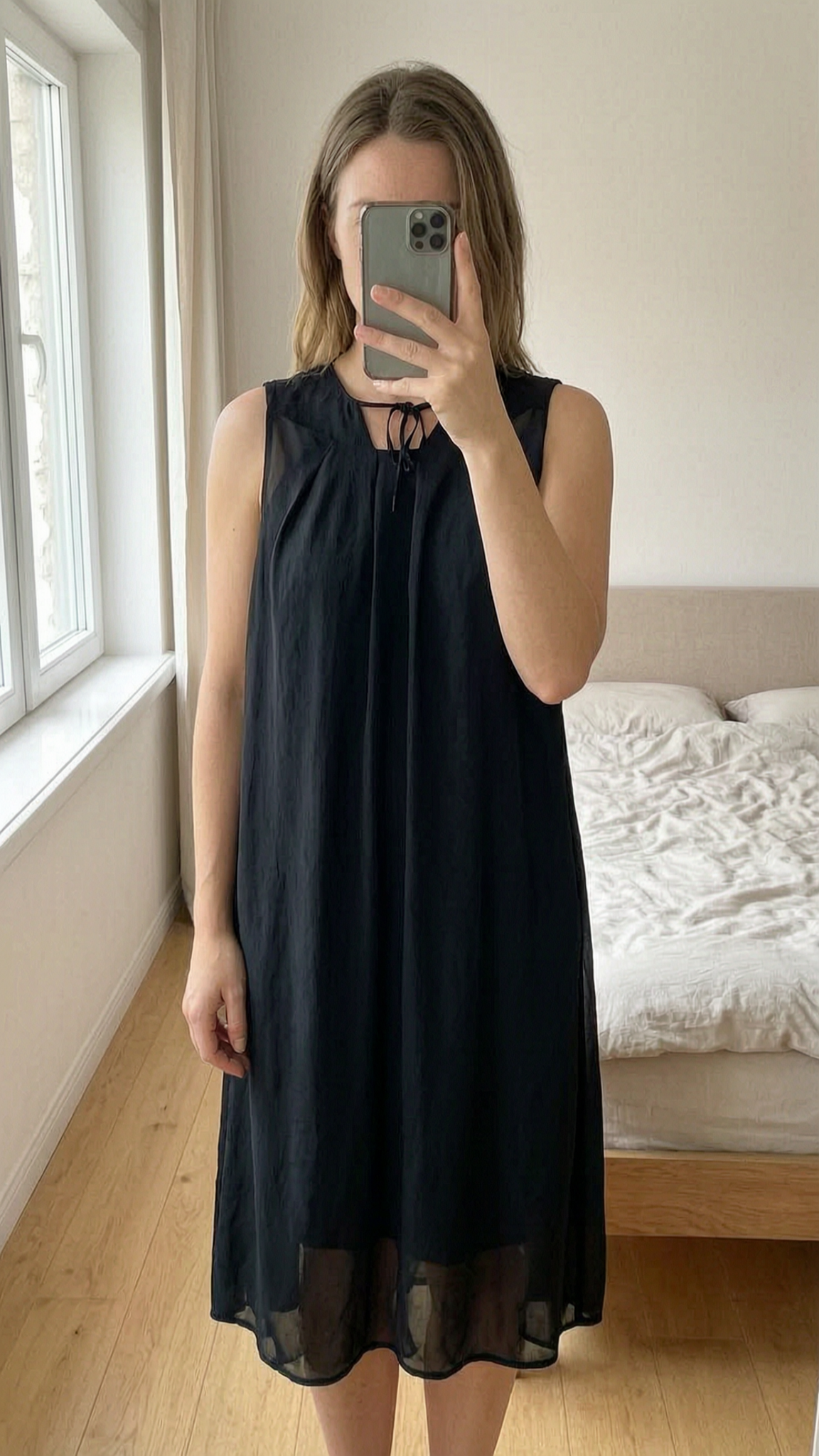 Robe fluide noir etam debout, face à la caméra, dans une chambre à la lumière douce, avec une lumière naturelle filtrant par la fenêtre.