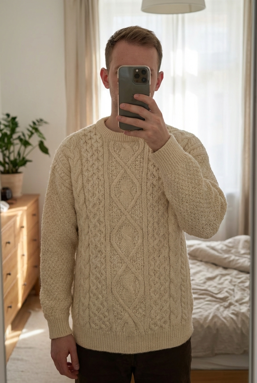 Pull Fait Main Tricot Aran Wool Sweater 100% Laine Beige Blanc Aran Craft M debout, face à la caméra, dans une chambre à la lumière douce, avec une lumière naturelle filtrant par la fenêtre.