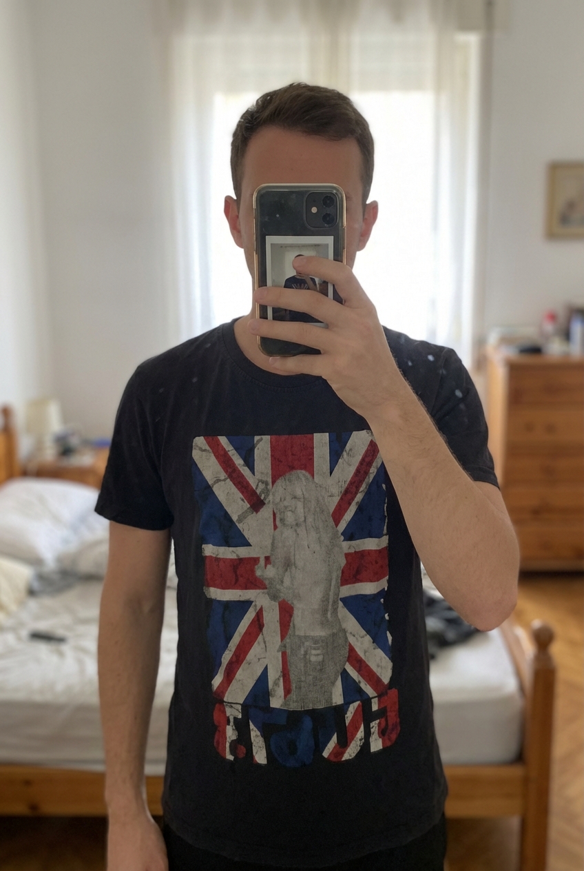 T Shirt America’s L debout, face à la caméra, dans une chambre à la lumière douce, avec une lumière naturelle filtrant par la fenêtre.