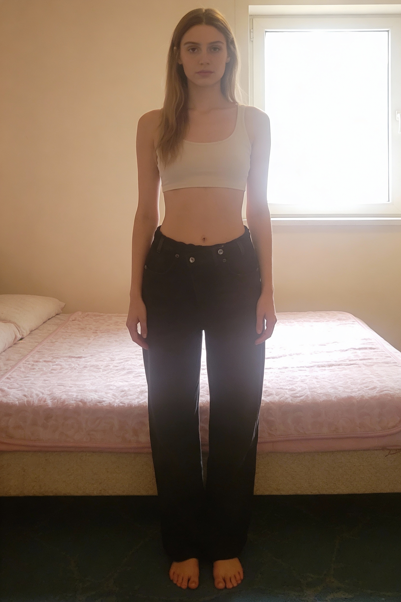 Pantalon noir denim taille haute XS – Neuf debout, face à la caméra, dans une chambre à la lumière douce, avec une lumière naturelle filtrant par la fenêtre.