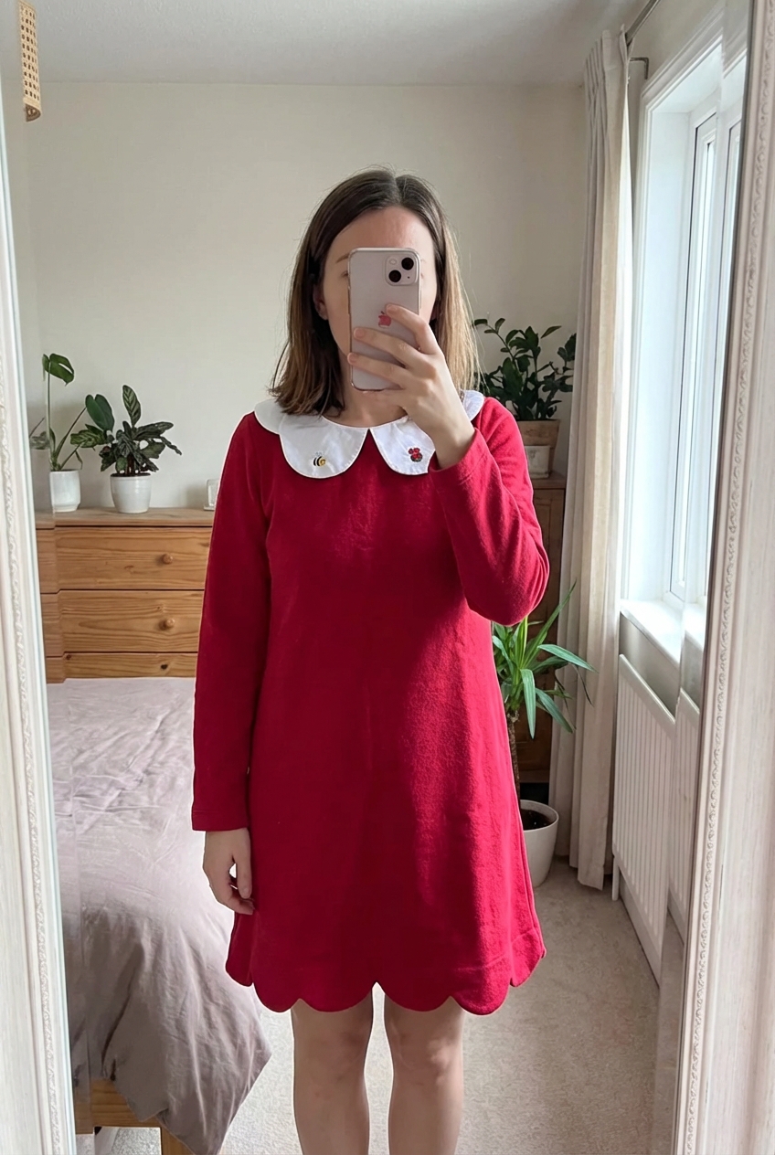 Vestido rojo Jacadi de pie, mirando a la cámara, en un dormitorio con luz suave y natural filtrándose por la ventana.