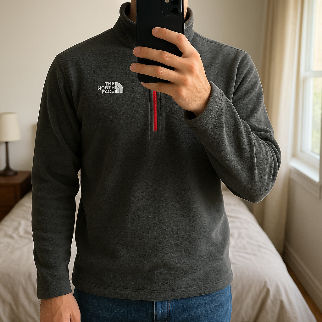 Veste Polaire Quarterzip The North Face gris S debout, face à la caméra, dans une chambre à la lumière douce, avec une lumière naturelle filtrant par la fenêtre.