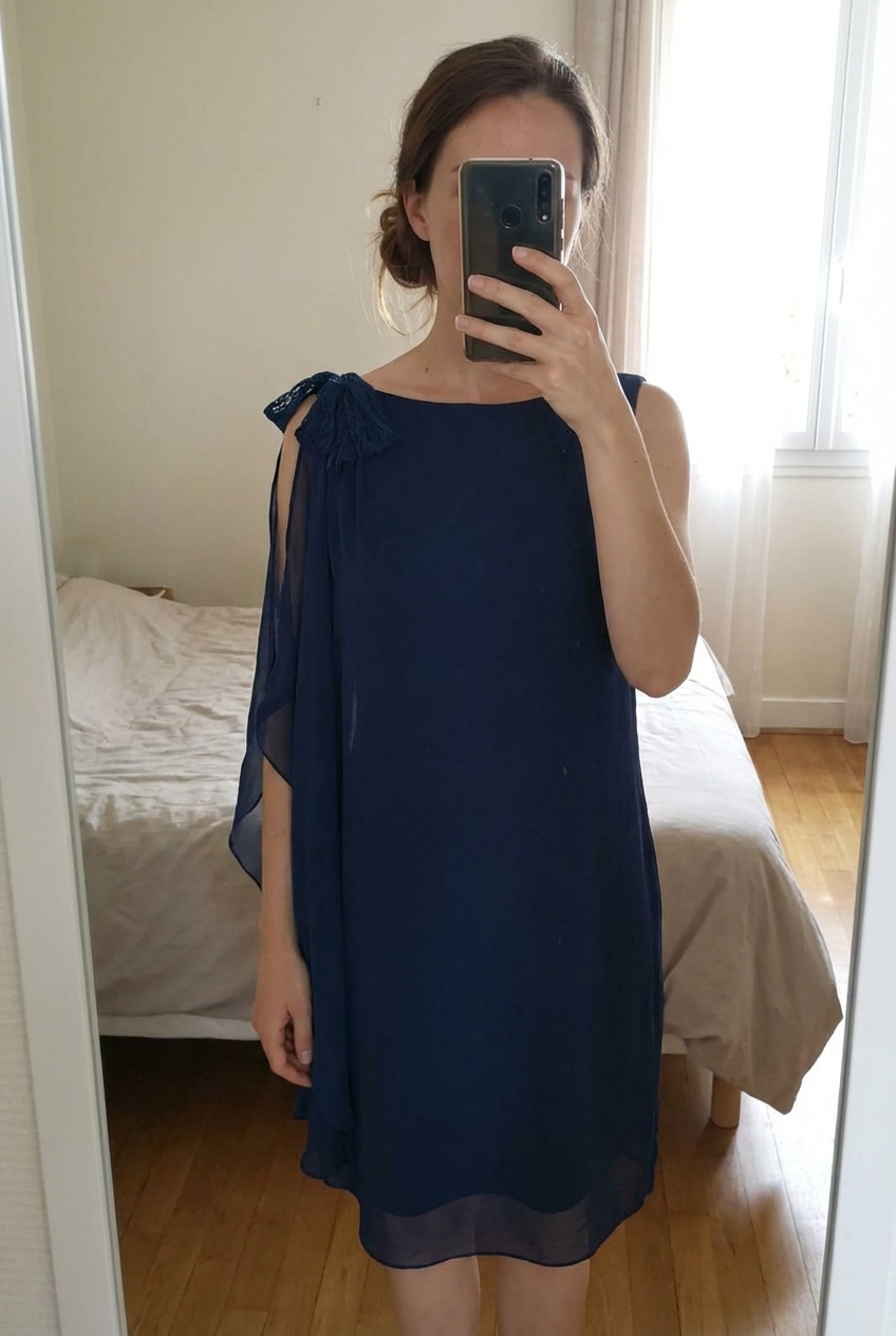 Sublime robe 36 debout, face à la caméra, dans une chambre à la lumière douce, avec une lumière naturelle filtrant par la fenêtre.