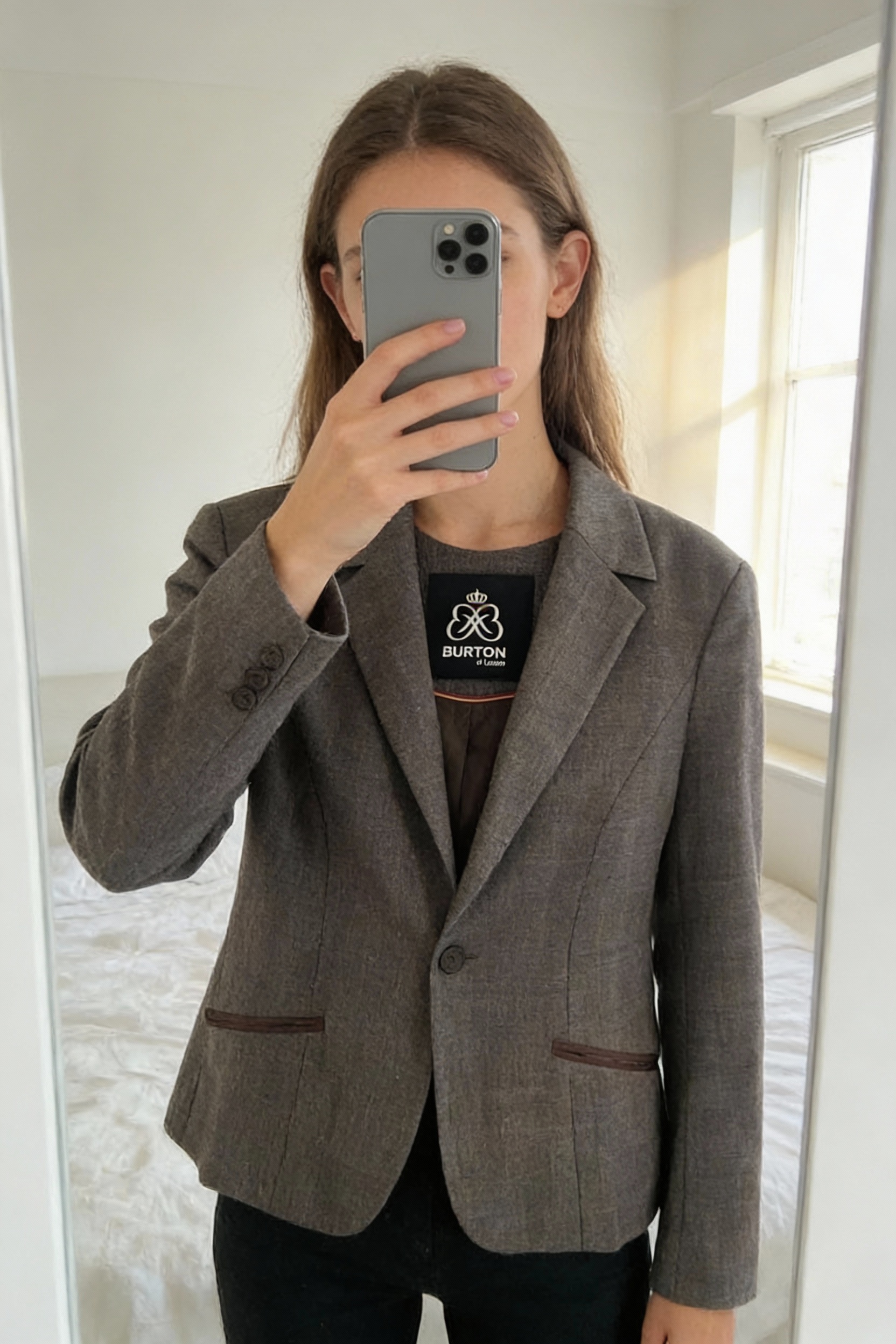 Veste Femme de marque Burton of London debout, face à la caméra, dans une chambre à la lumière douce, avec une lumière naturelle filtrant par la fenêtre.