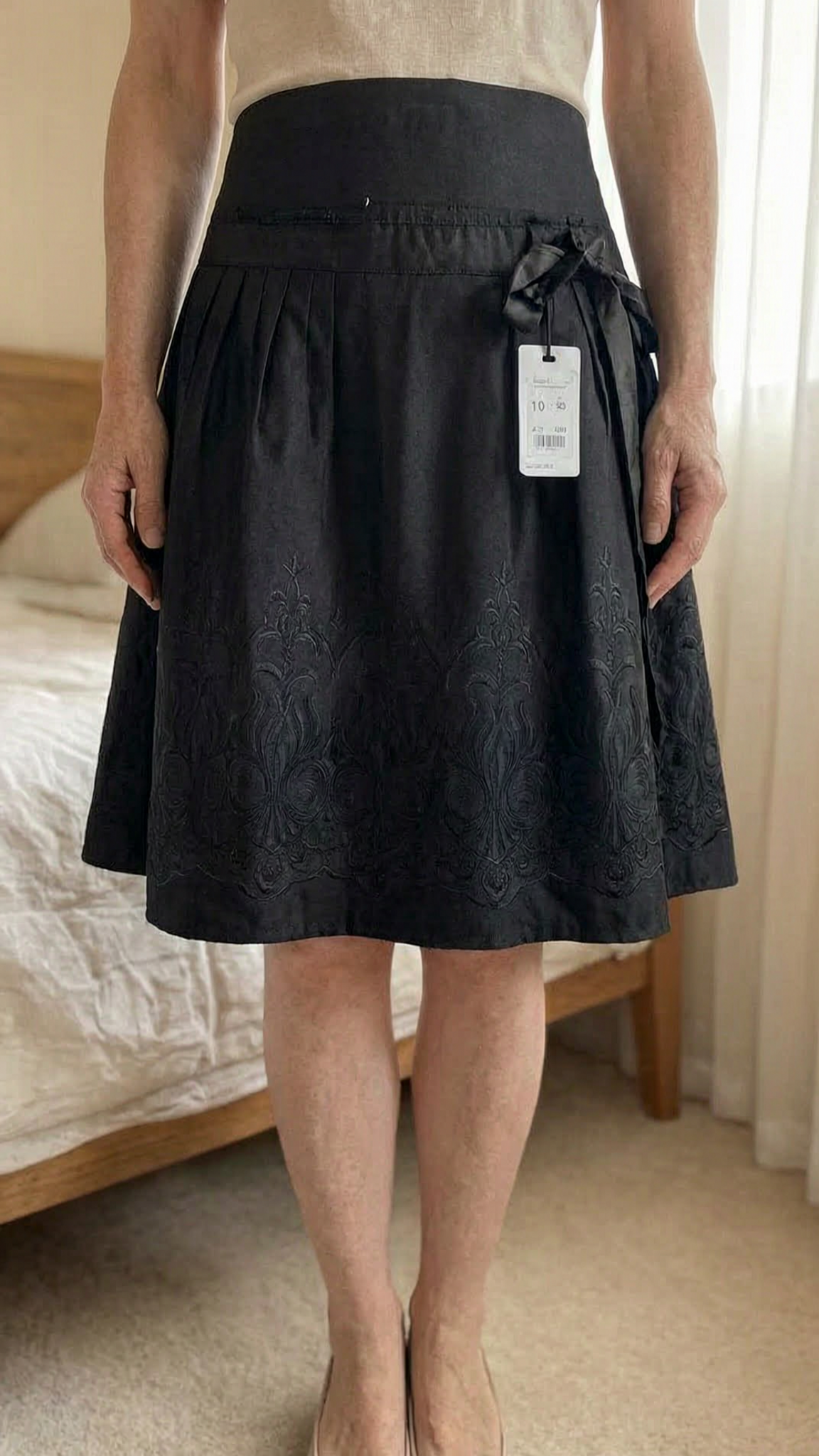 New Look black cotton skirt with embroidery size 10 New with tags standing straight facing the camera, in a softly lit bedroom setting, with gentle natural light filtering through a window.
