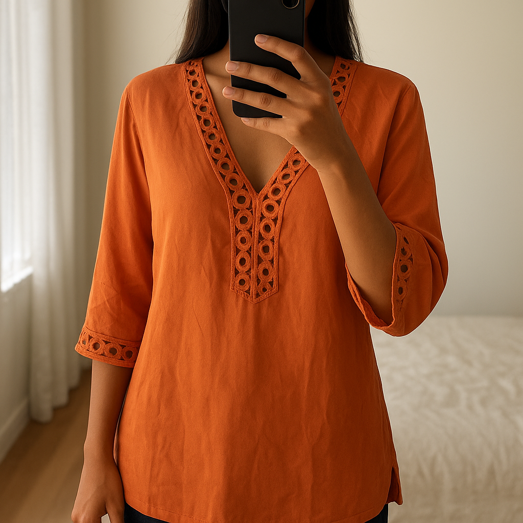 Une personne en Tunique Chicme satiné orange debout, face à la caméra, avec une silhouette fine, dans une chambre à la lumière douce, avec une lumière naturelle filtrant par la fenêtre.