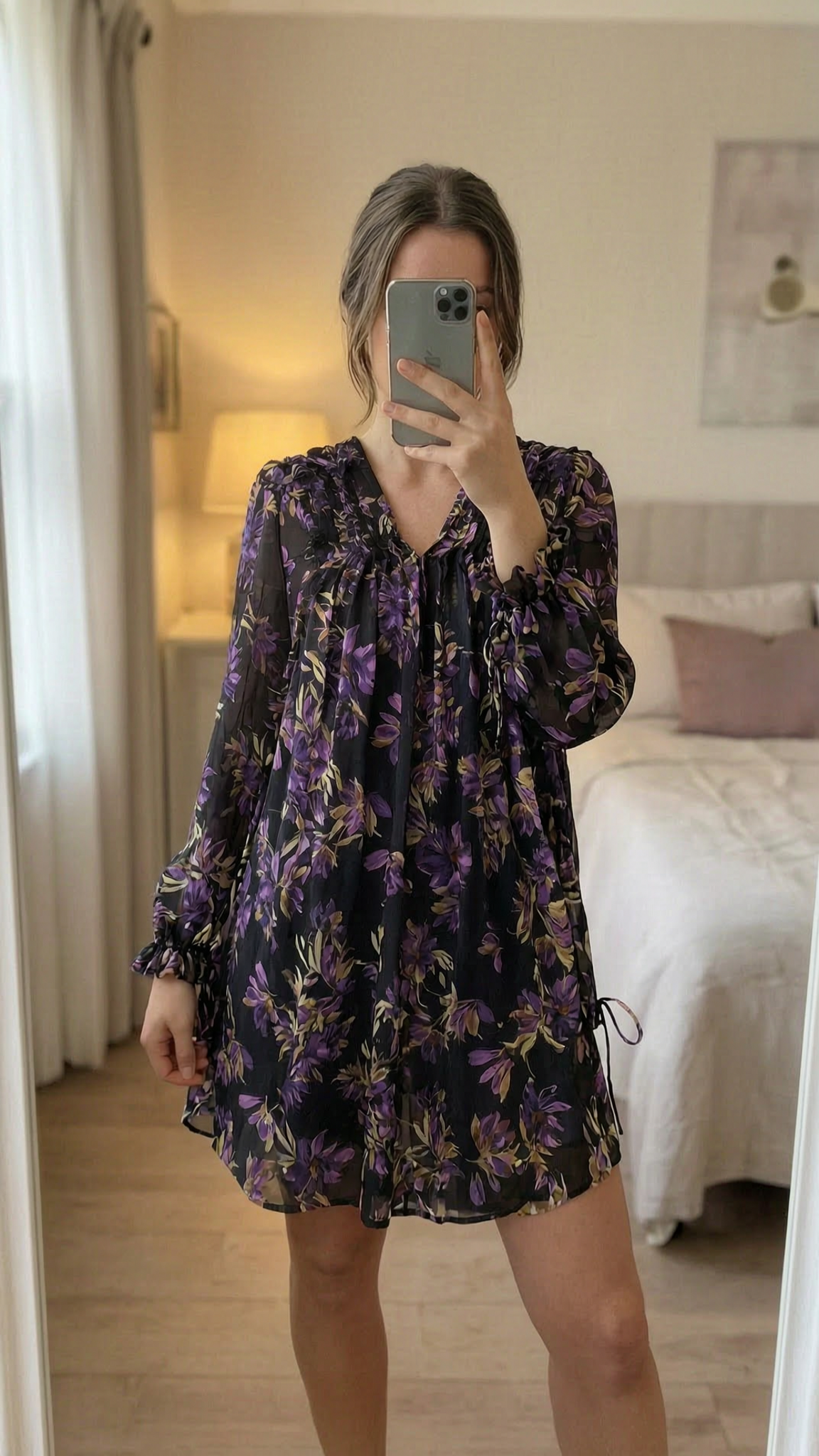 Robe manches longues Guess debout, face à la caméra, dans une chambre à la lumière douce, avec une lumière naturelle filtrant par la fenêtre.