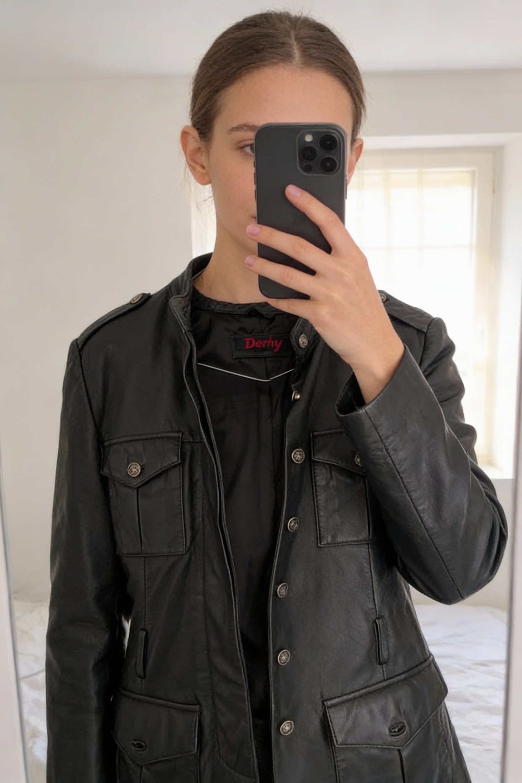 Veste Femme perfecto Cuir femme debout, face à la caméra, dans une chambre à la lumière douce, avec une lumière naturelle filtrant par la fenêtre.