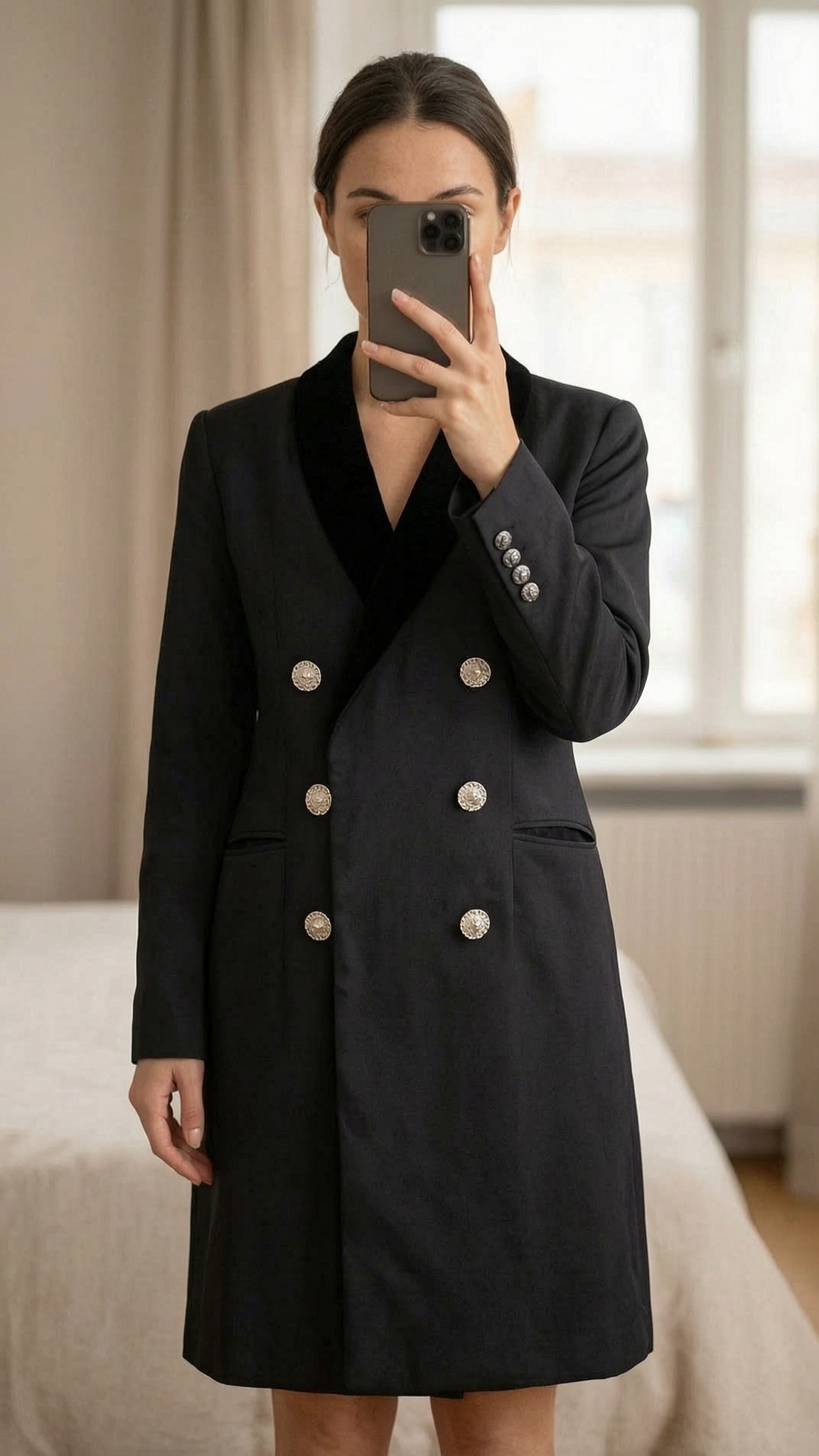 Veste légère ou robe The Kooples, taille 34 debout, face à la caméra, dans une chambre à la lumière douce, avec une lumière naturelle filtrant par la fenêtre.