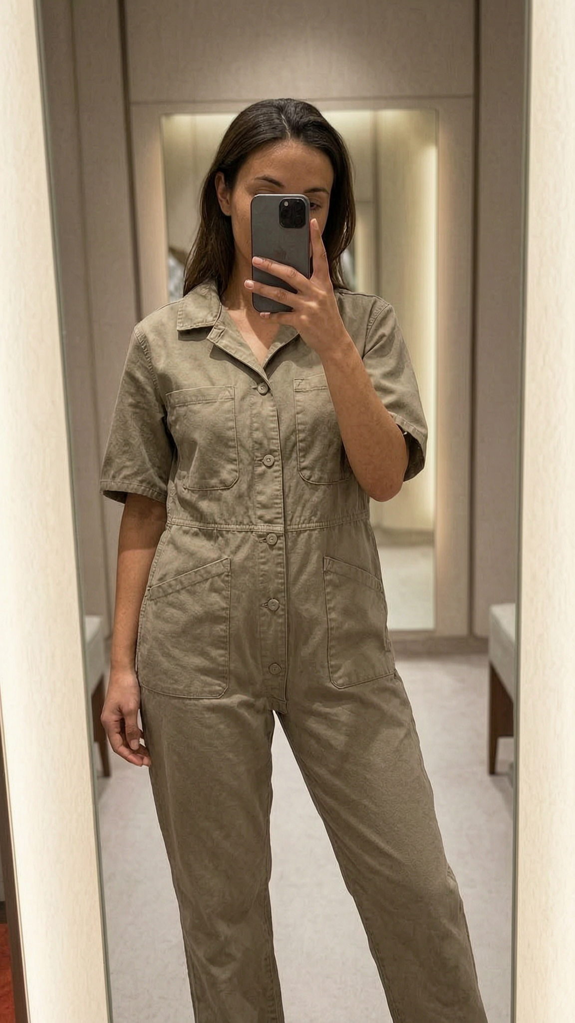 Une personne en Combi cambrant légèrement le dos pour une pose dynamique, dans une cabine d’essayage de style boutique avec un miroir et une décoration neutre.