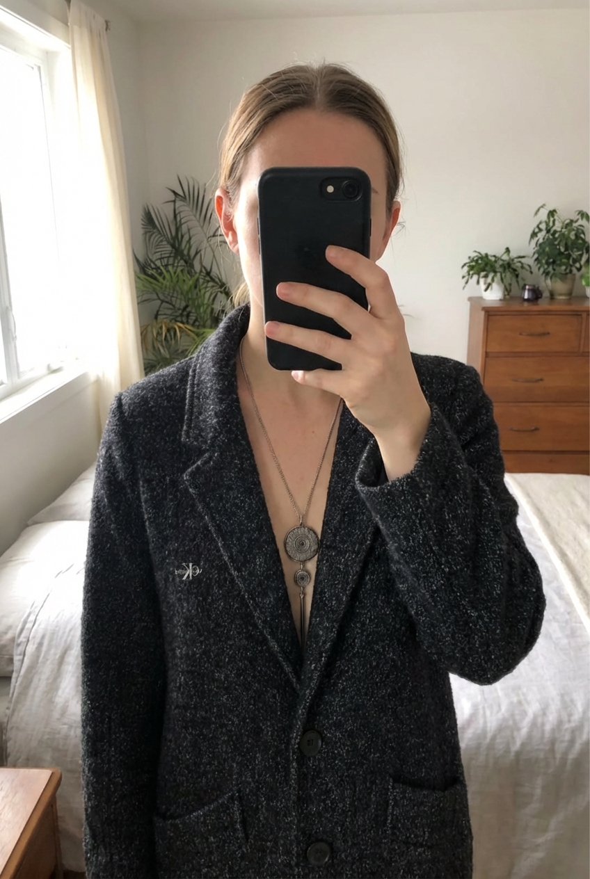 Manteau Calvin Klein T38 debout, face à la caméra, dans une chambre à la lumière douce, avec une lumière naturelle filtrant par la fenêtre.