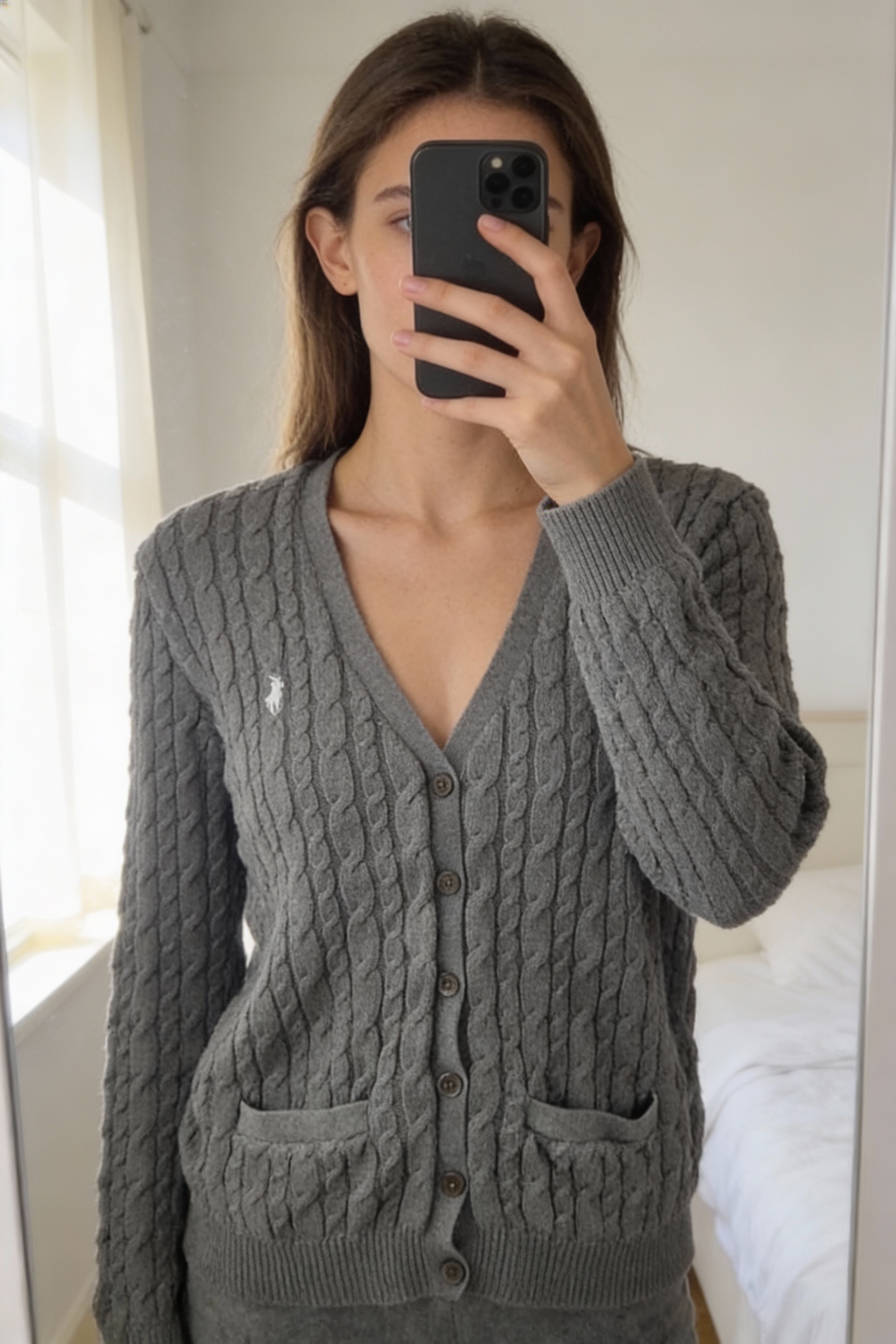 Gilet cardigan Ralph lauren femme torsadé gris taille L 40 debout, face à la caméra, dans une chambre à la lumière douce, avec une lumière naturelle filtrant par la fenêtre.