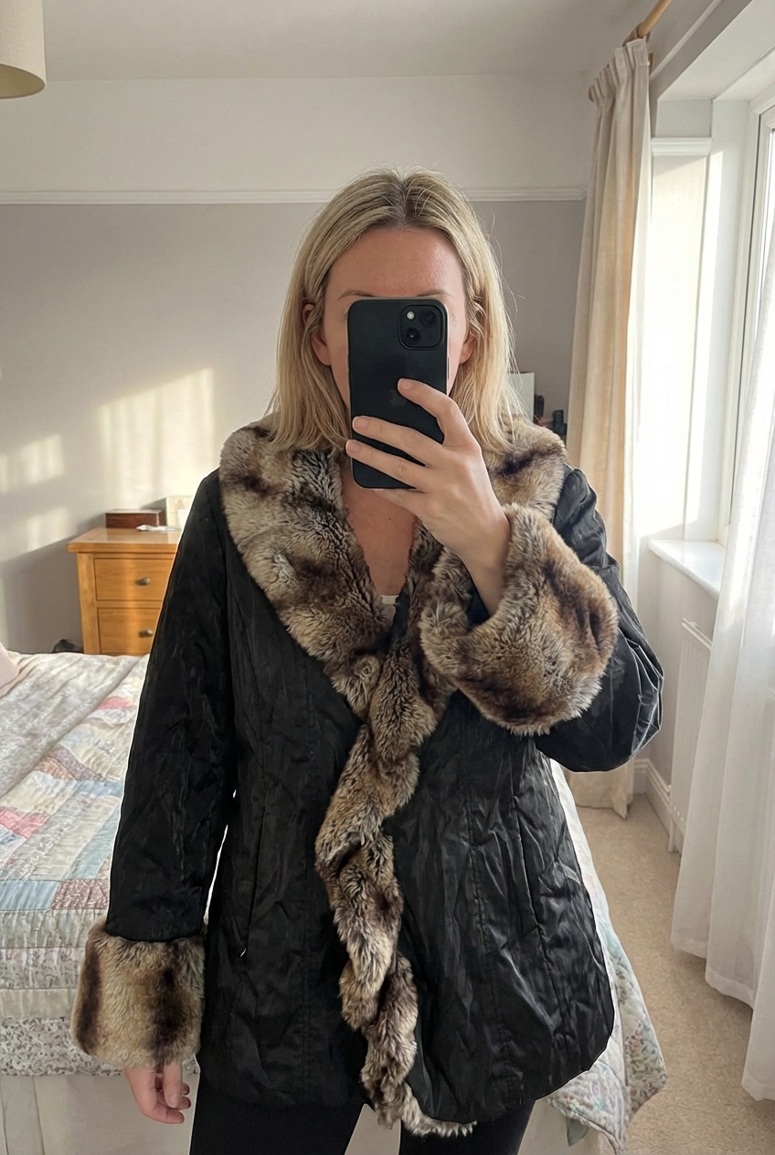 A person in Vintage Y2K per Una black brown faux fur coat standing straight facing the camera, in a softly lit bedroom setting, with gentle natural light filtering through a window.