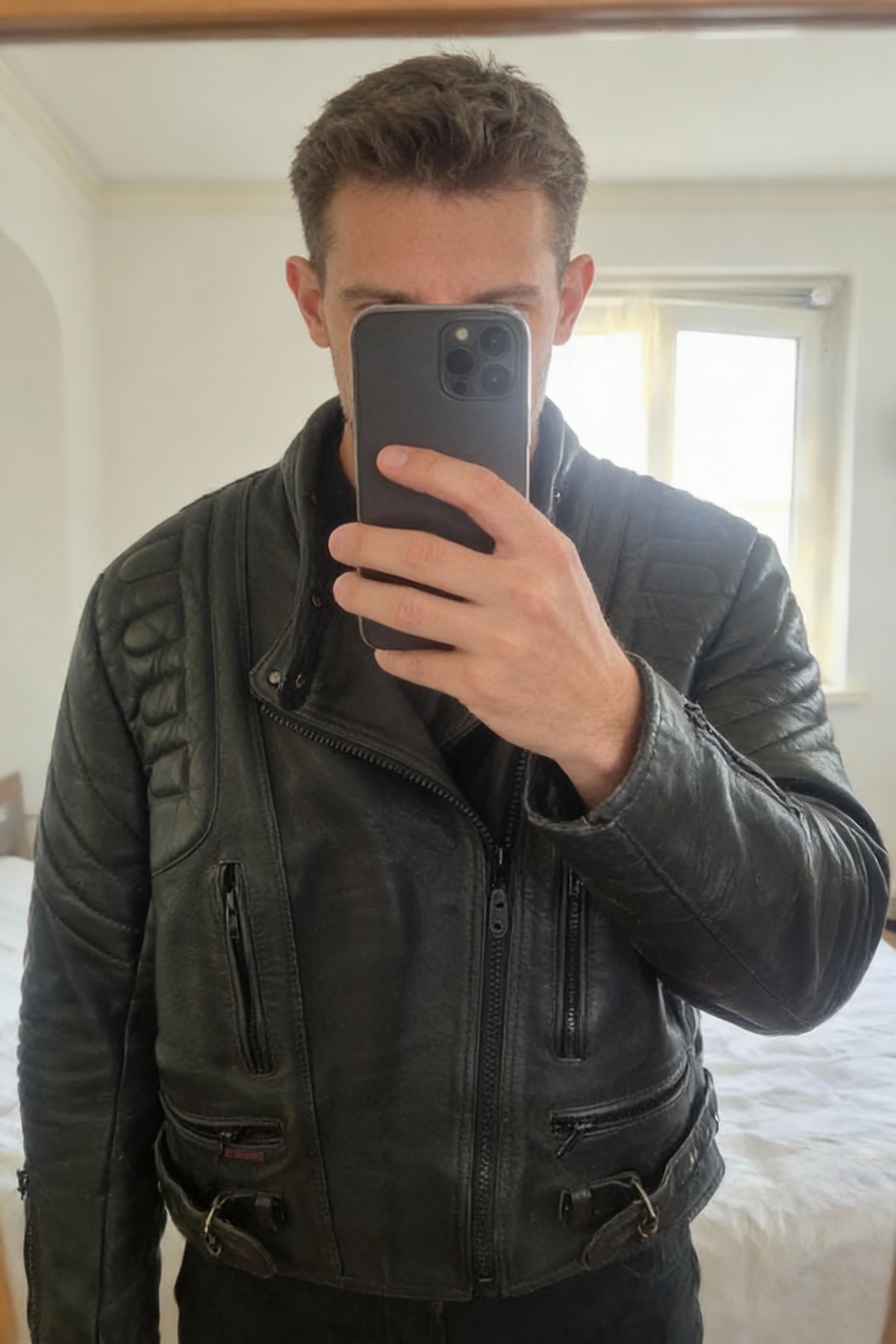 Cuir moto femme debout, face à la caméra, dans une chambre à la lumière douce, avec une lumière naturelle filtrant par la fenêtre.