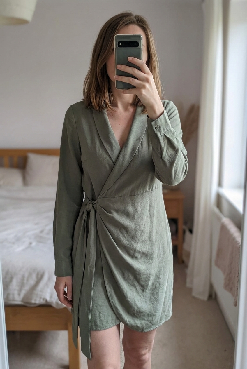 Wunderschönes, geschmeidiges Kleid zum Wickeln | Gr. 36 aufrecht stehend, der Kamera zugewandt, in einem sanft beleuchteten Schlafzimmer, mit natürlichem Licht, das durch ein Fenster fällt.