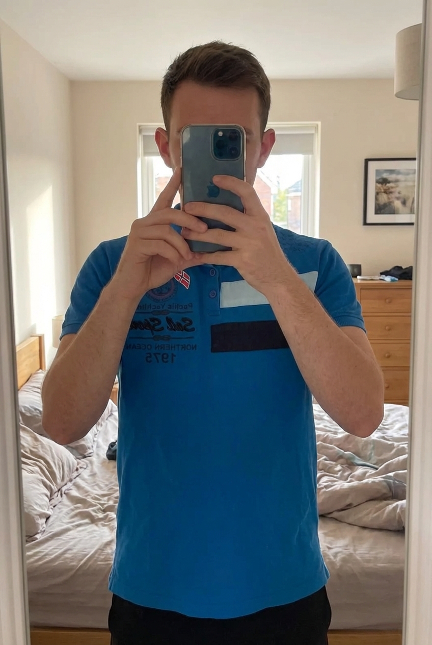 Polo homme yachting taille s debout, face à la caméra, dans une chambre à la lumière douce, avec une lumière naturelle filtrant par la fenêtre.