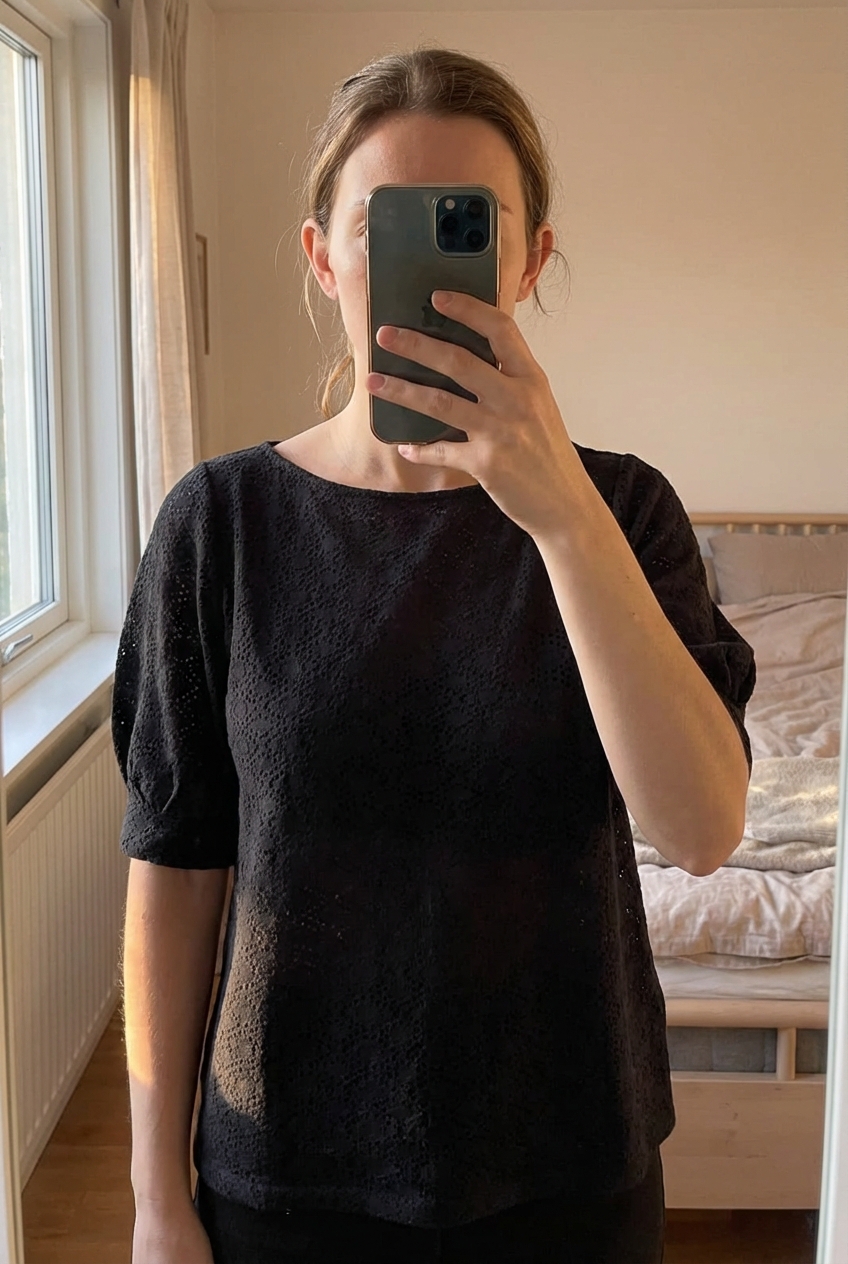 Tee shirt femme transparente promod taille 40 debout, face à la caméra, dans une chambre à la lumière douce, avec une lumière naturelle filtrant par la fenêtre.