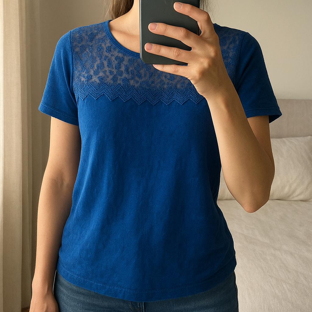 Tee-shirt The Kooples bleu taille S debout, face à la caméra, dans une chambre à la lumière douce, avec une lumière naturelle filtrant par la fenêtre.