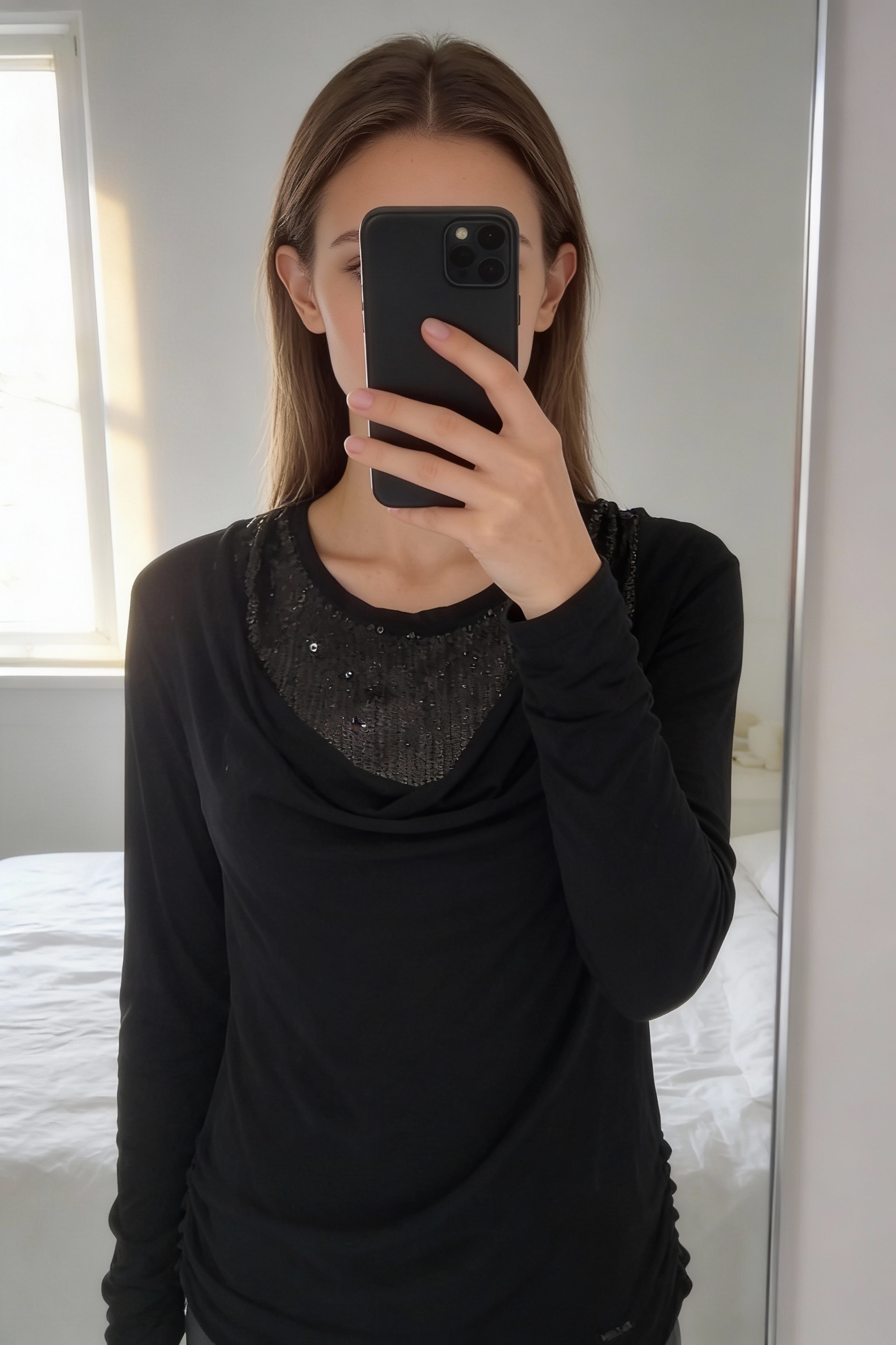 Khujo noir sequin M neuf debout, face à la caméra, dans une chambre à la lumière douce, avec une lumière naturelle filtrant par la fenêtre.