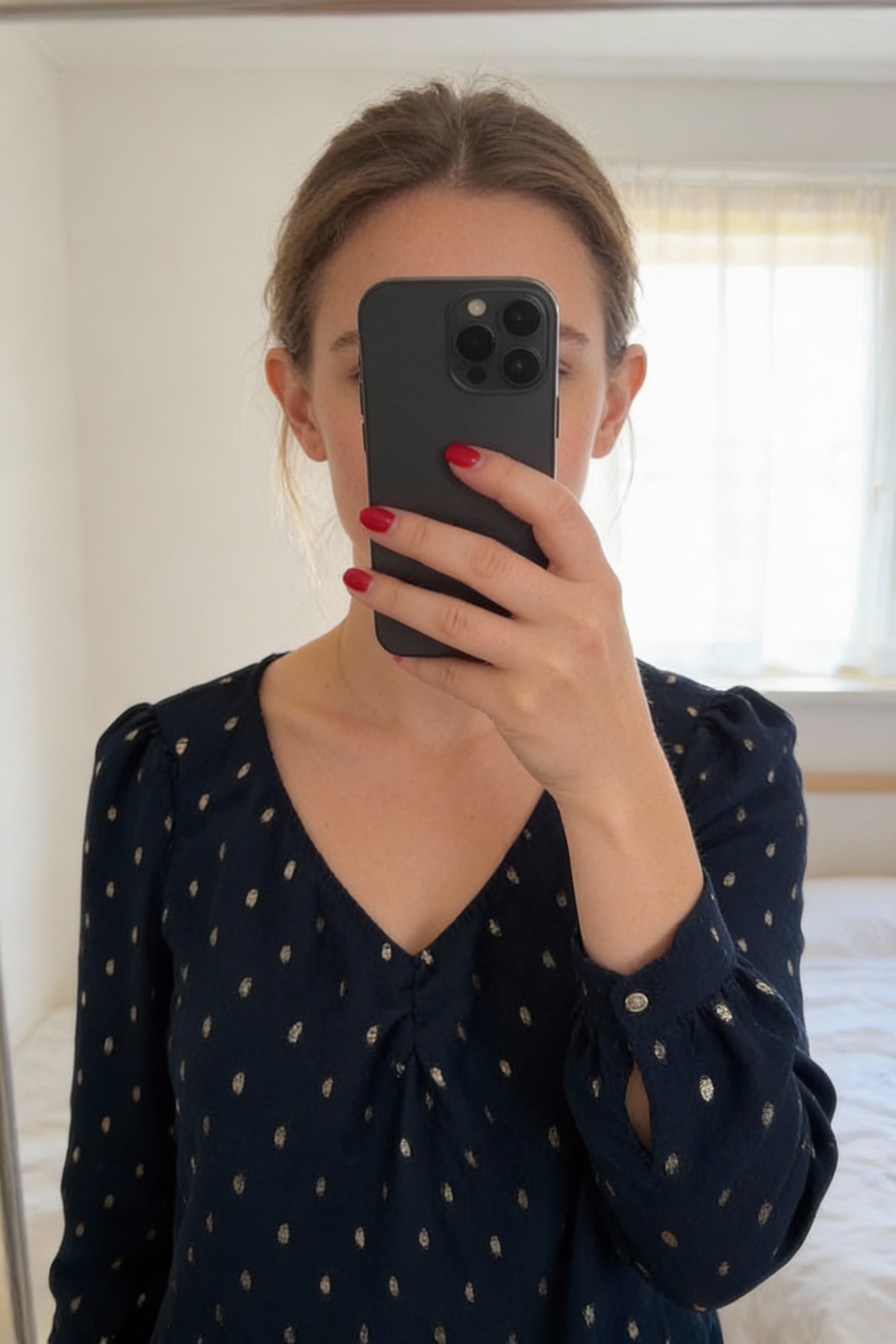 Blouse bleu nuit naf naf debout, face à la caméra, dans une chambre à la lumière douce, avec une lumière naturelle filtrant par la fenêtre.