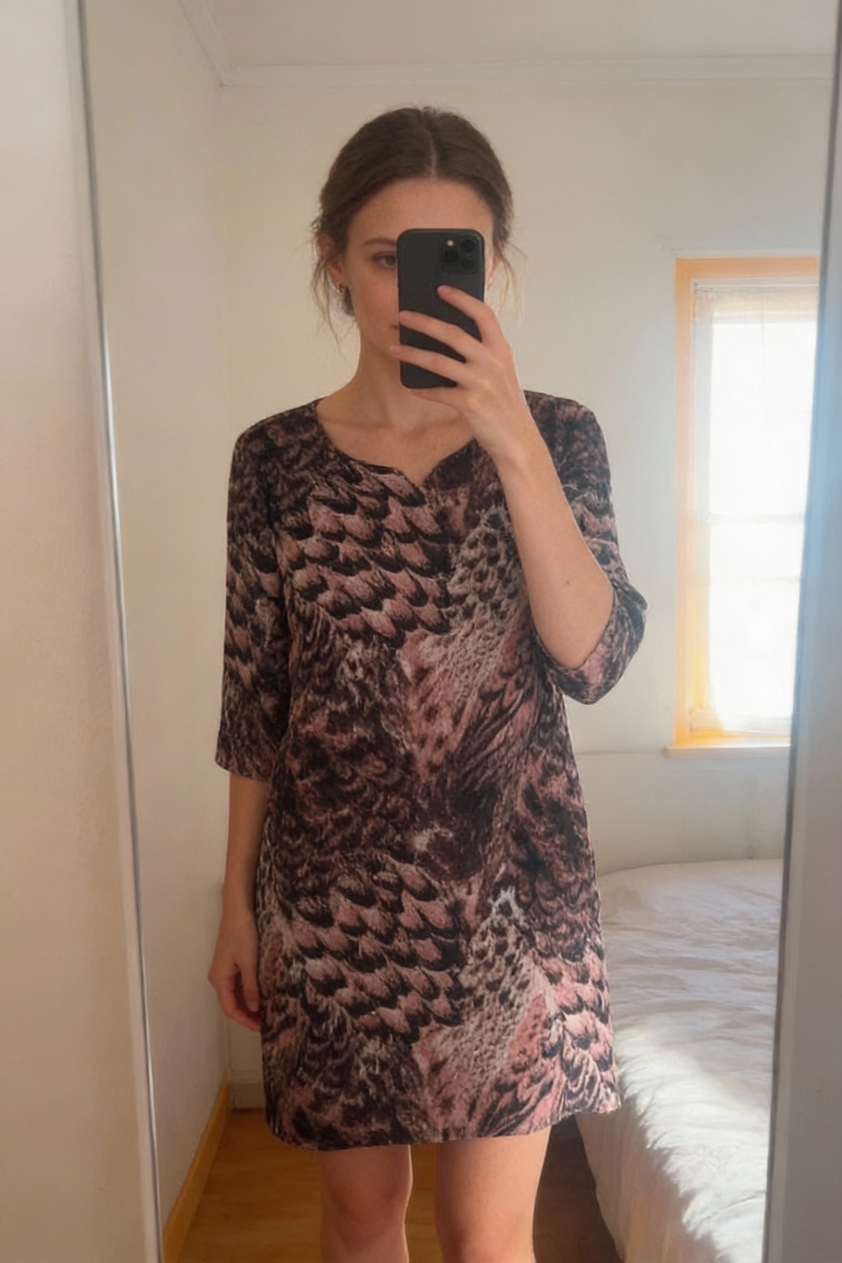 Robe panthère rose debout, face à la caméra, dans une chambre à la lumière douce, avec une lumière naturelle filtrant par la fenêtre.