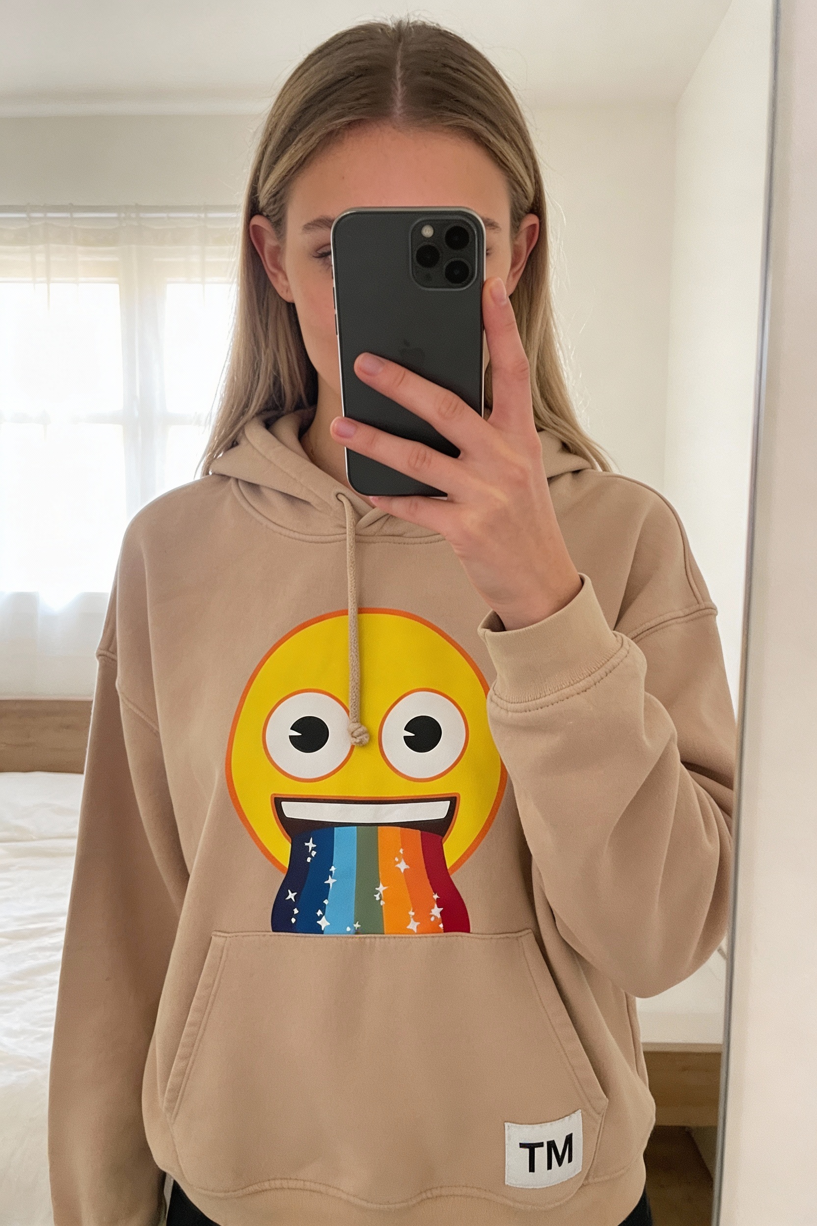 Sweet a capuche femme emoji taille S debout, face à la caméra, dans une chambre à la lumière douce, avec une lumière naturelle filtrant par la fenêtre.