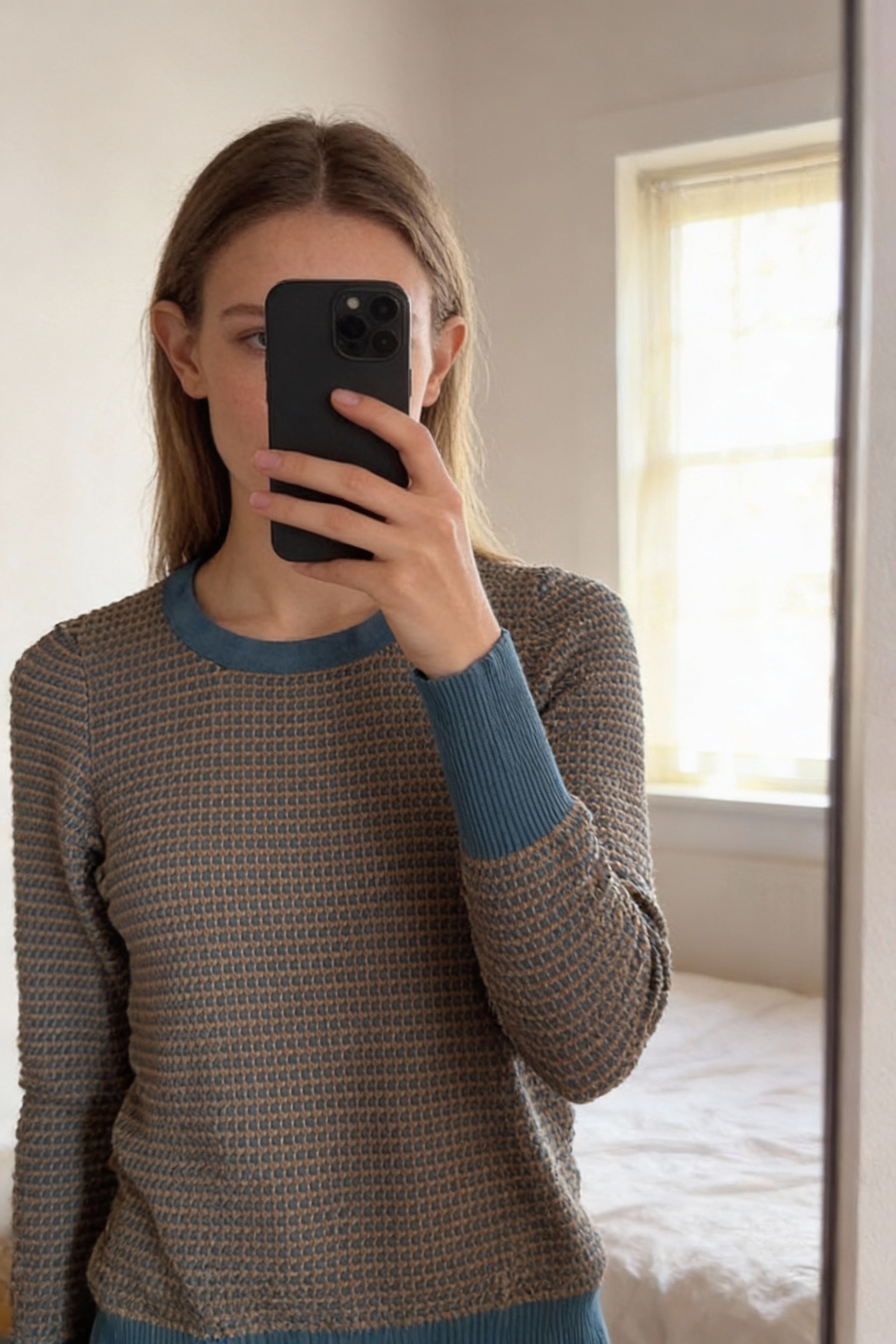 Una persona in Pull moulant Zara M bleu marron - Maglione Zara donna M in piedi, rivolto verso la fotocamera, in una camera da letto con luce soffusa e luce naturale che filtra dalla finestra.